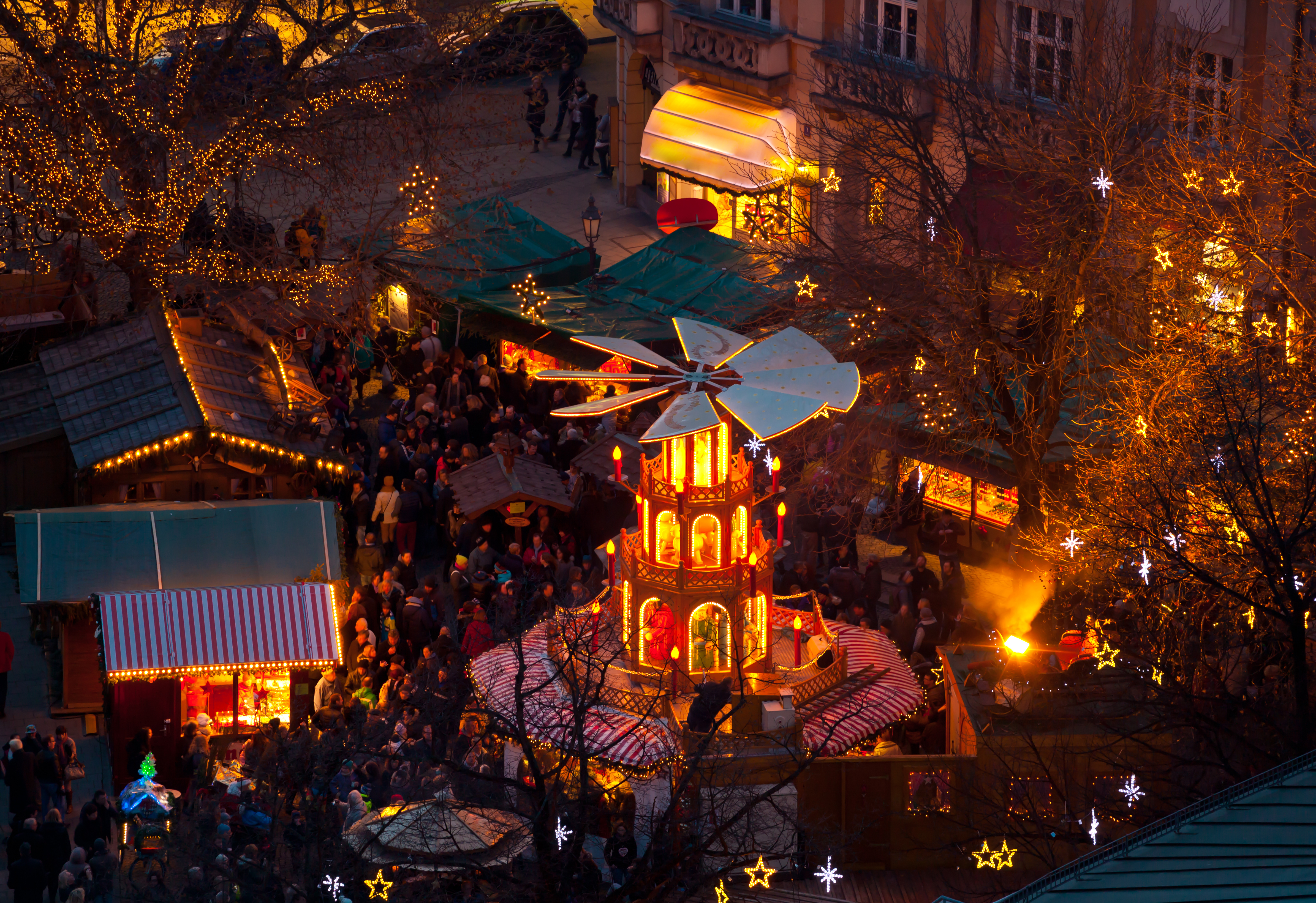 Mercado navideño nocturno con pirámide iluminada, puestos y gente.
