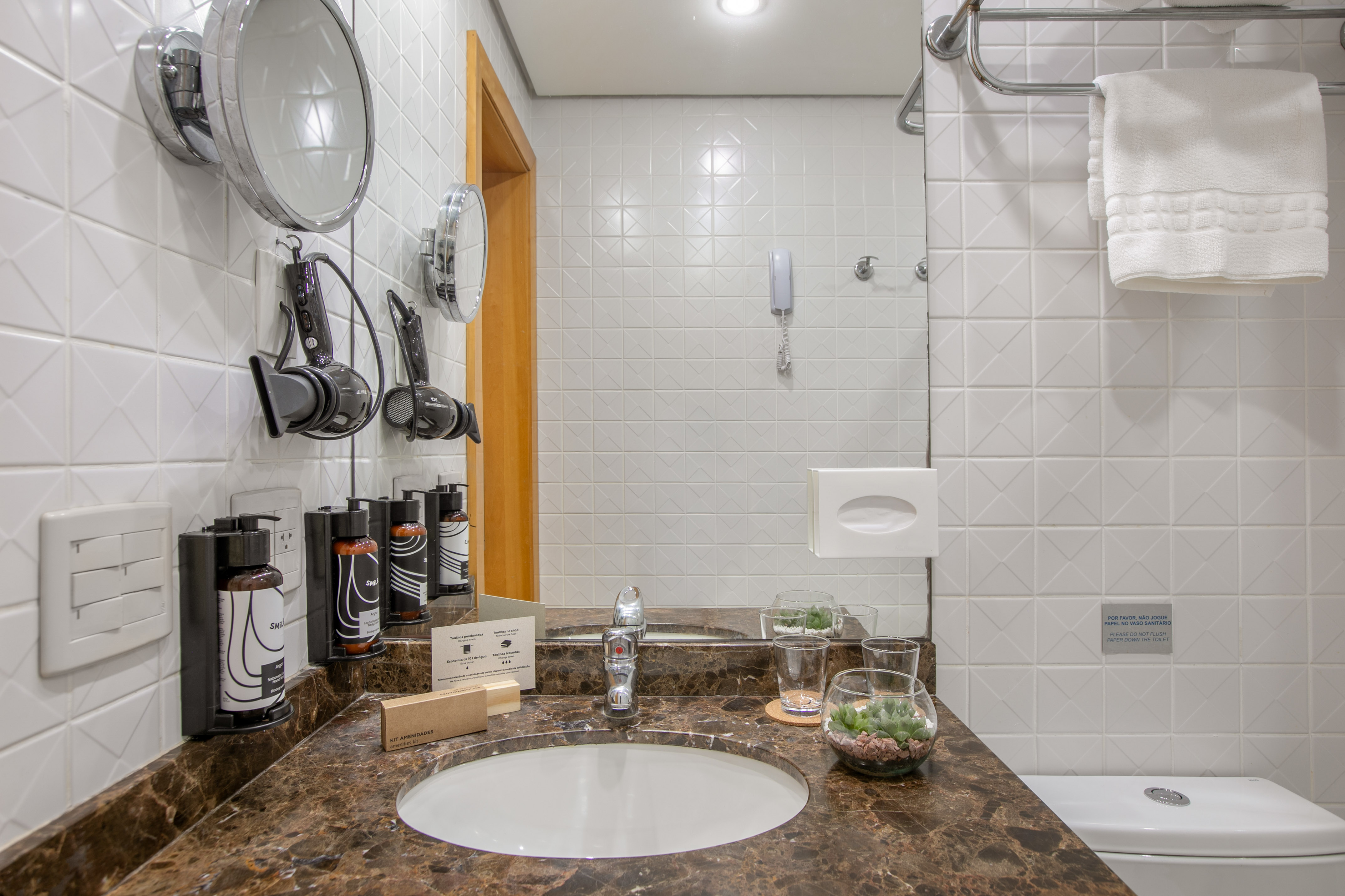 Hotel bathroom: white tile walls, marble vanity, sink, dual mirrors, hair dryers. - The INNSiDE Triple Queen - INNSiDE São Paulo Higienópolis, Sao Paulo