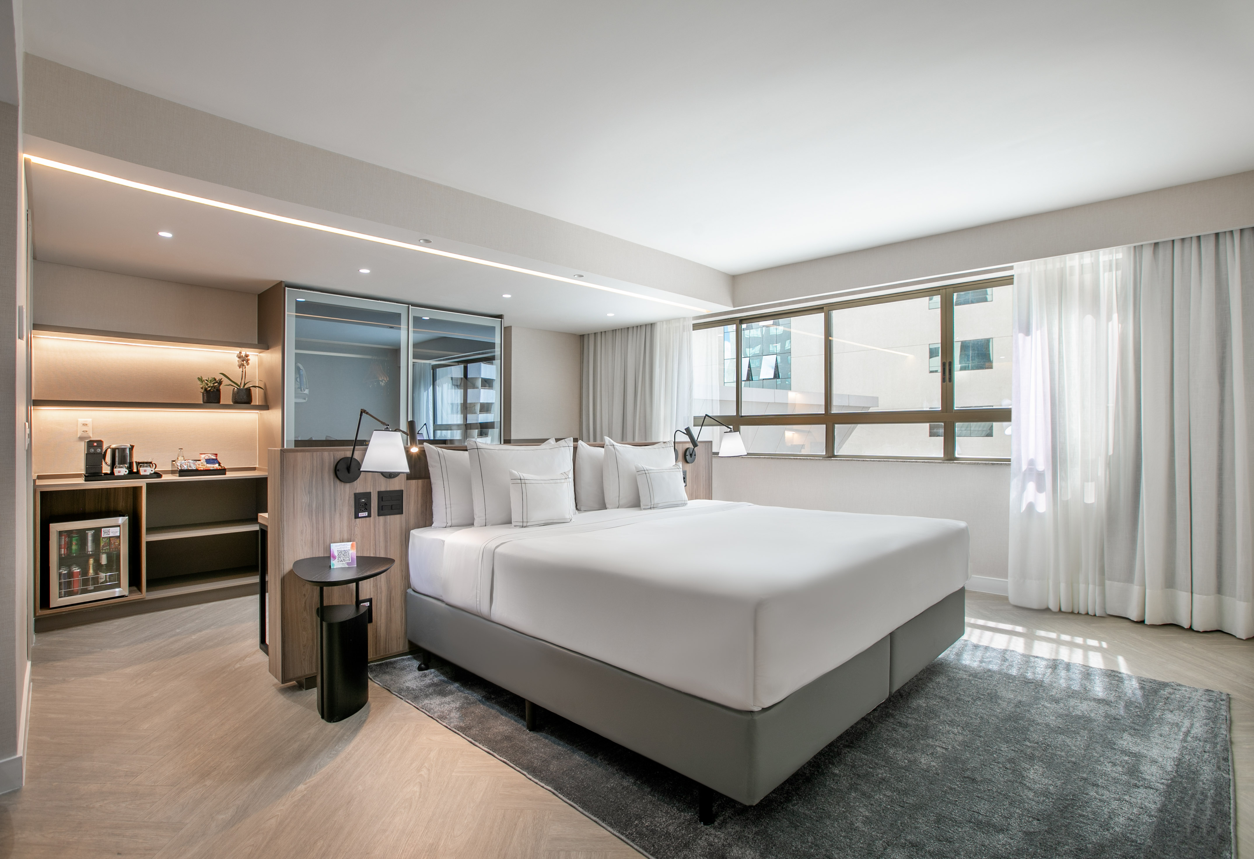Modern hotel room with king bed, large window, and coffee station.
