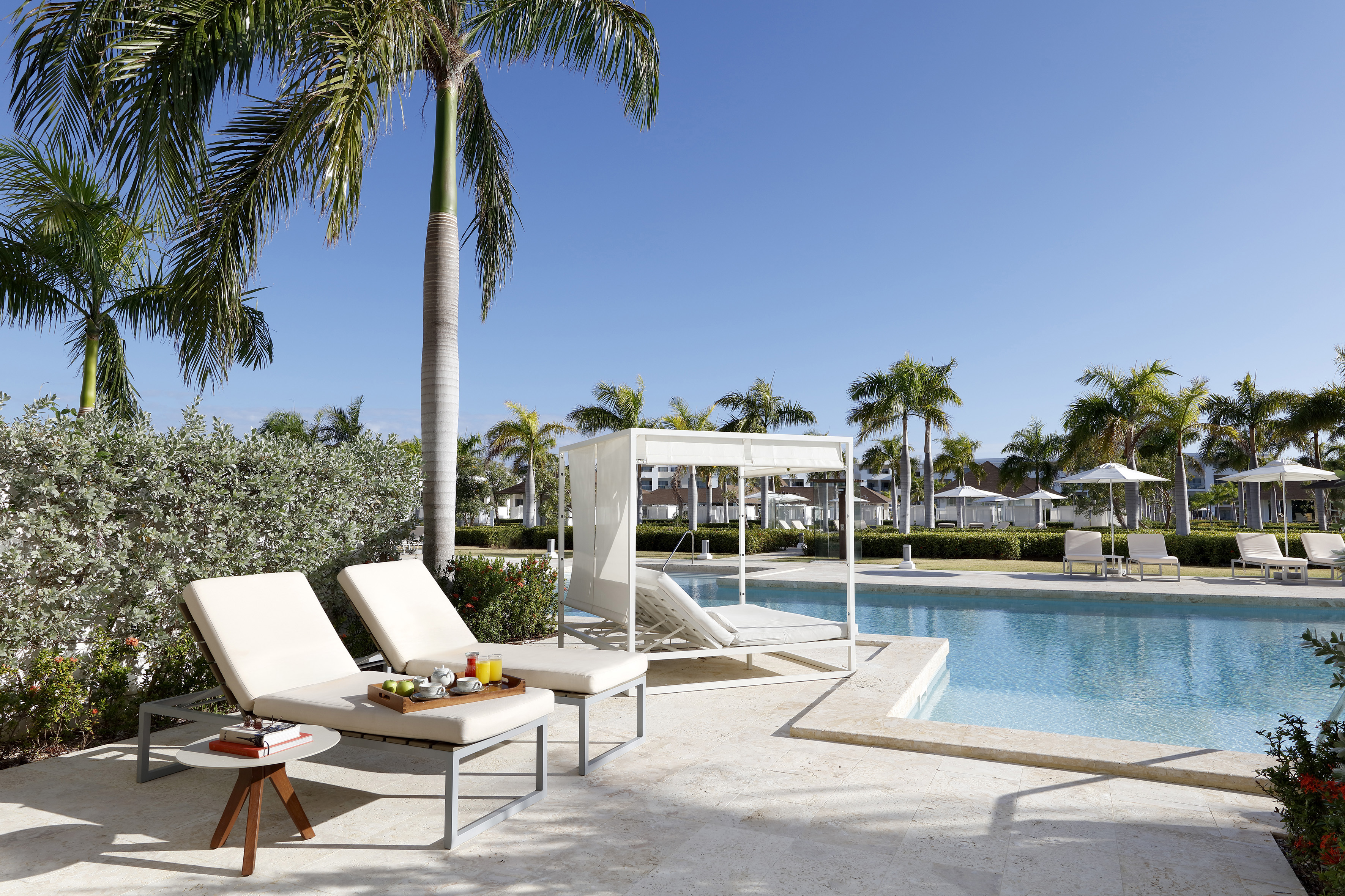 Luxury resort pool with palm trees, chaise lounges, and white canopy daybed.