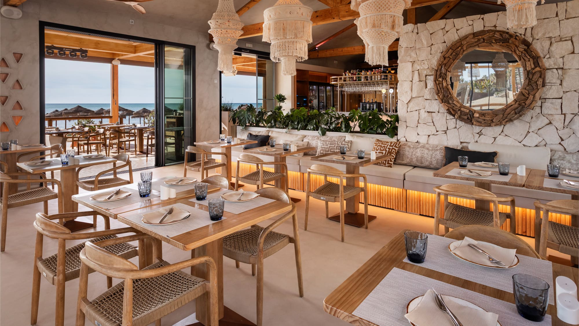 Beachfront restaurant with macrame chandeliers, wooden tables, and sea view.
