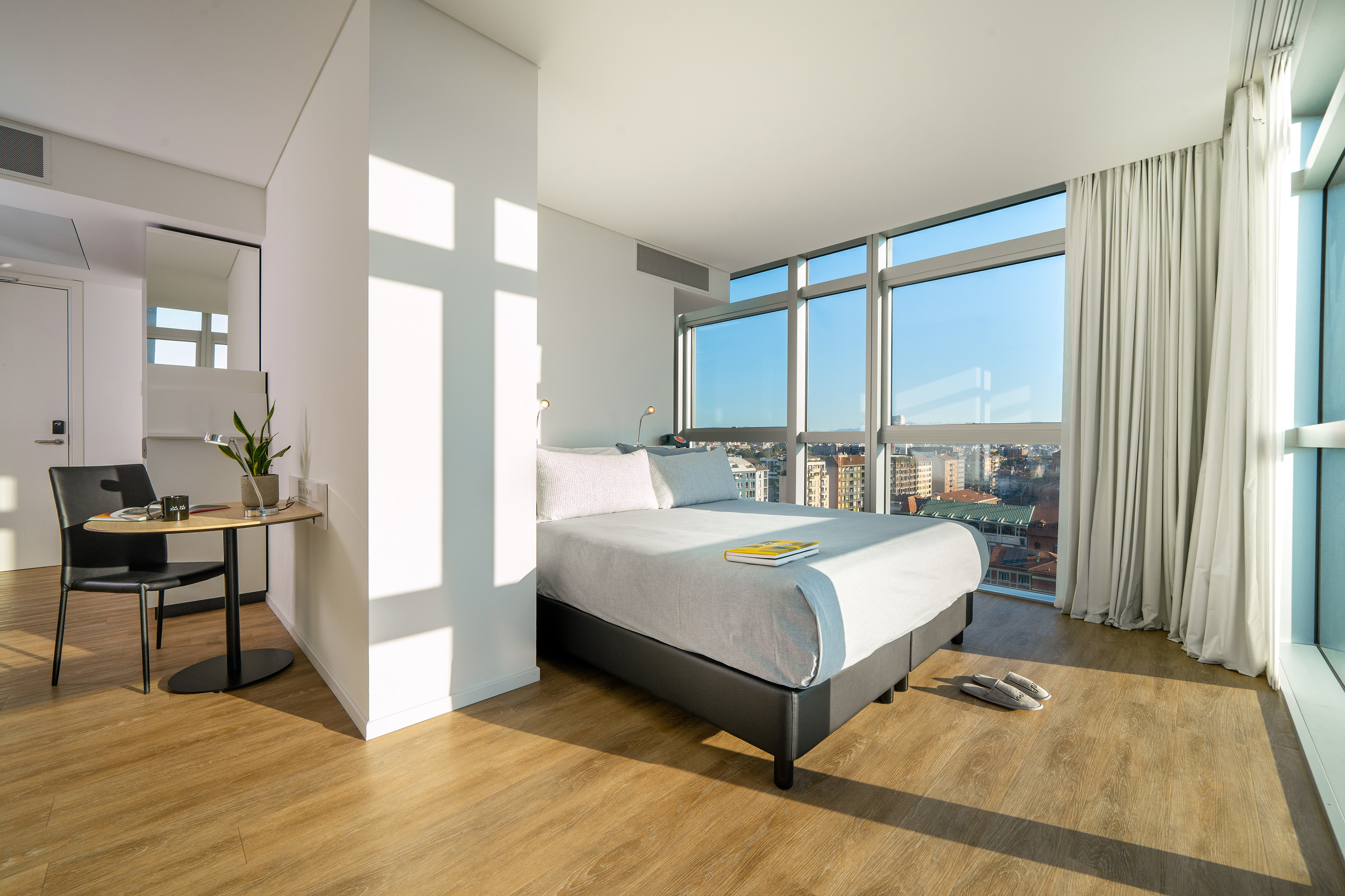 Modern hotel room with floor-to-ceiling windows overlooking city skyline.