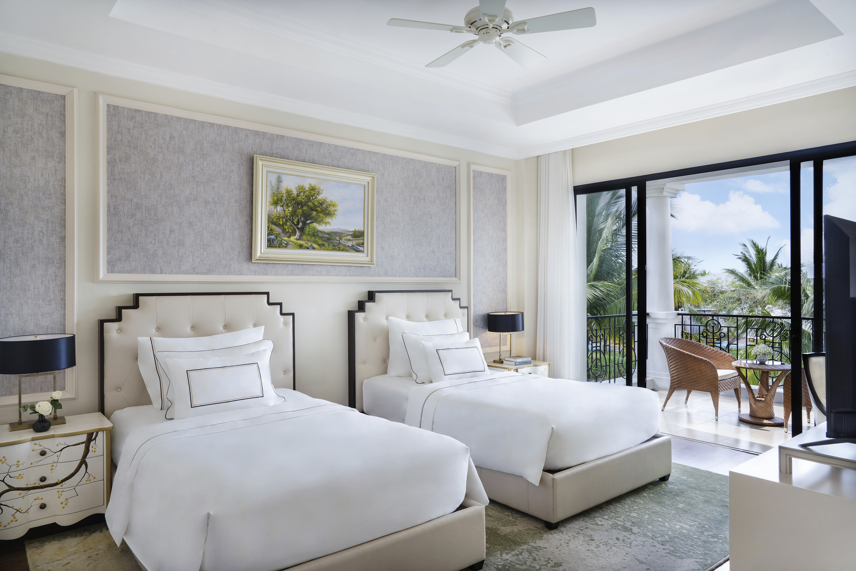 Elegant hotel room with twin beds, balcony, tropical resort view, ceiling fan.