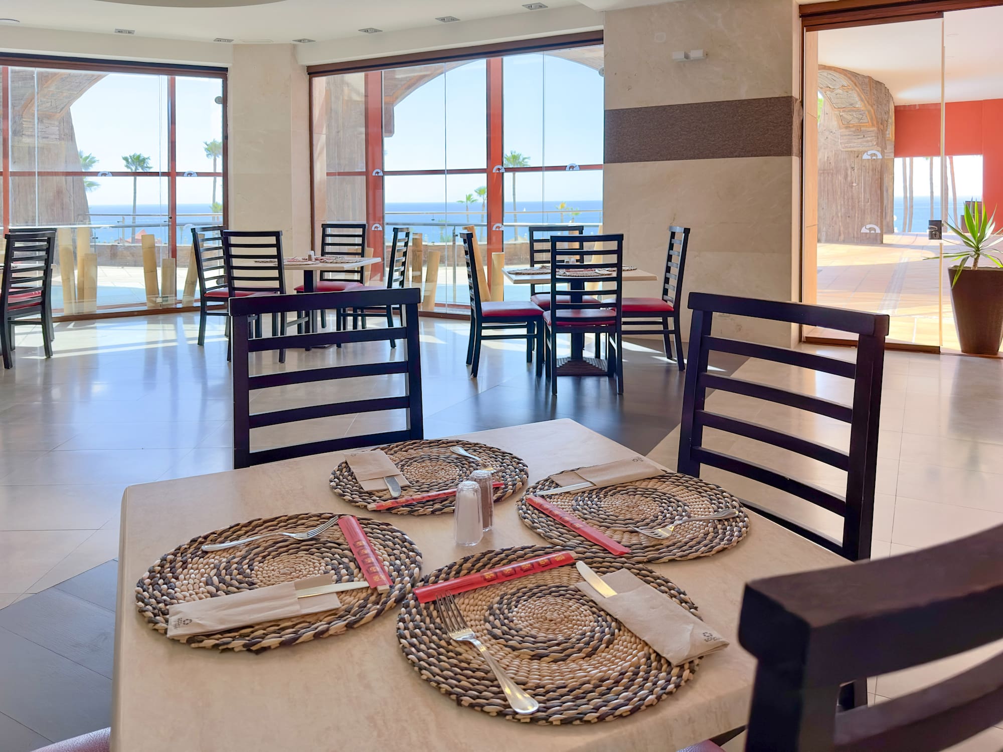 a table with place settings and chairs in a room with a view of the ocean