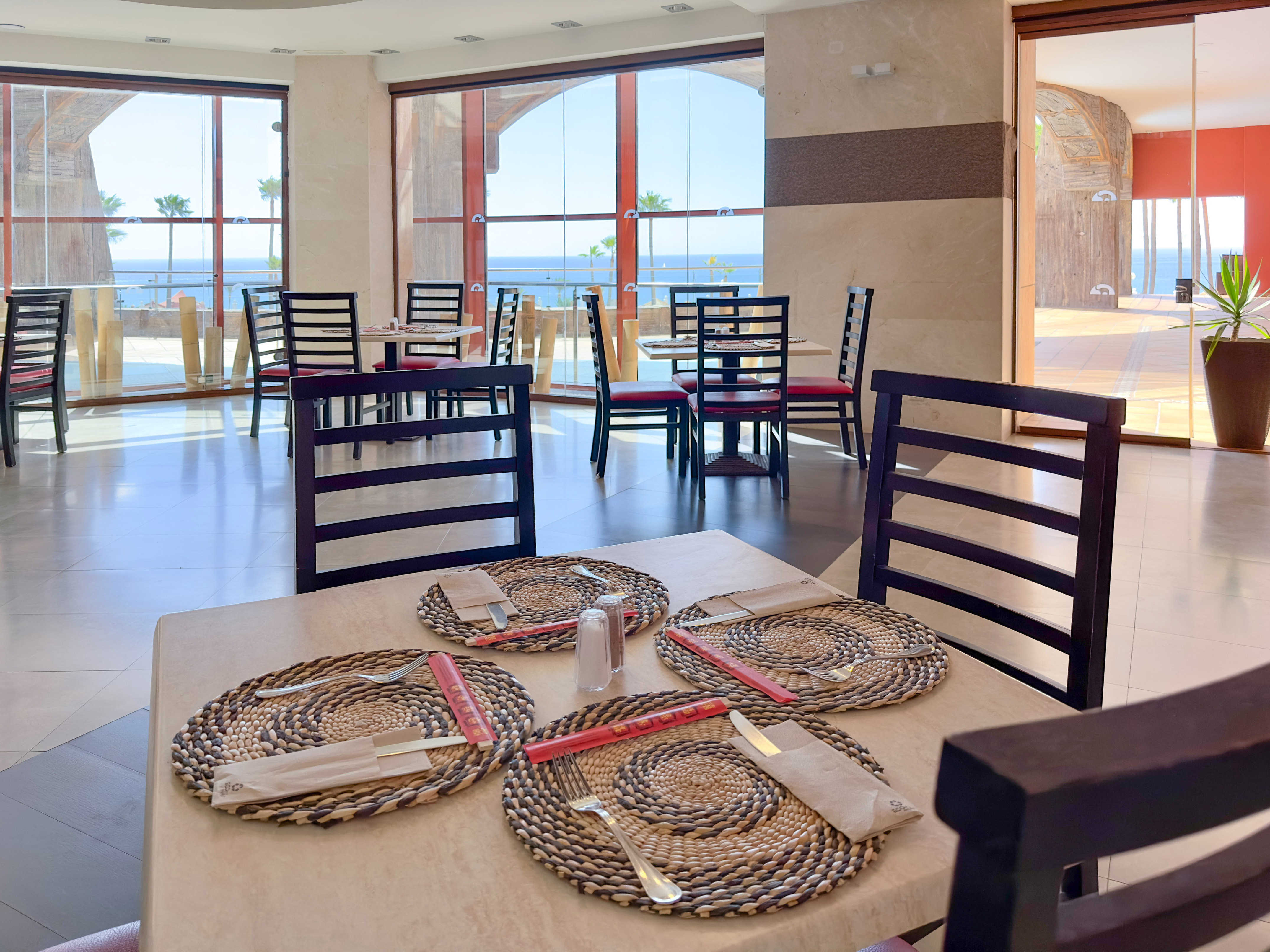 a table with place settings and chairs in a room with a view of the ocean