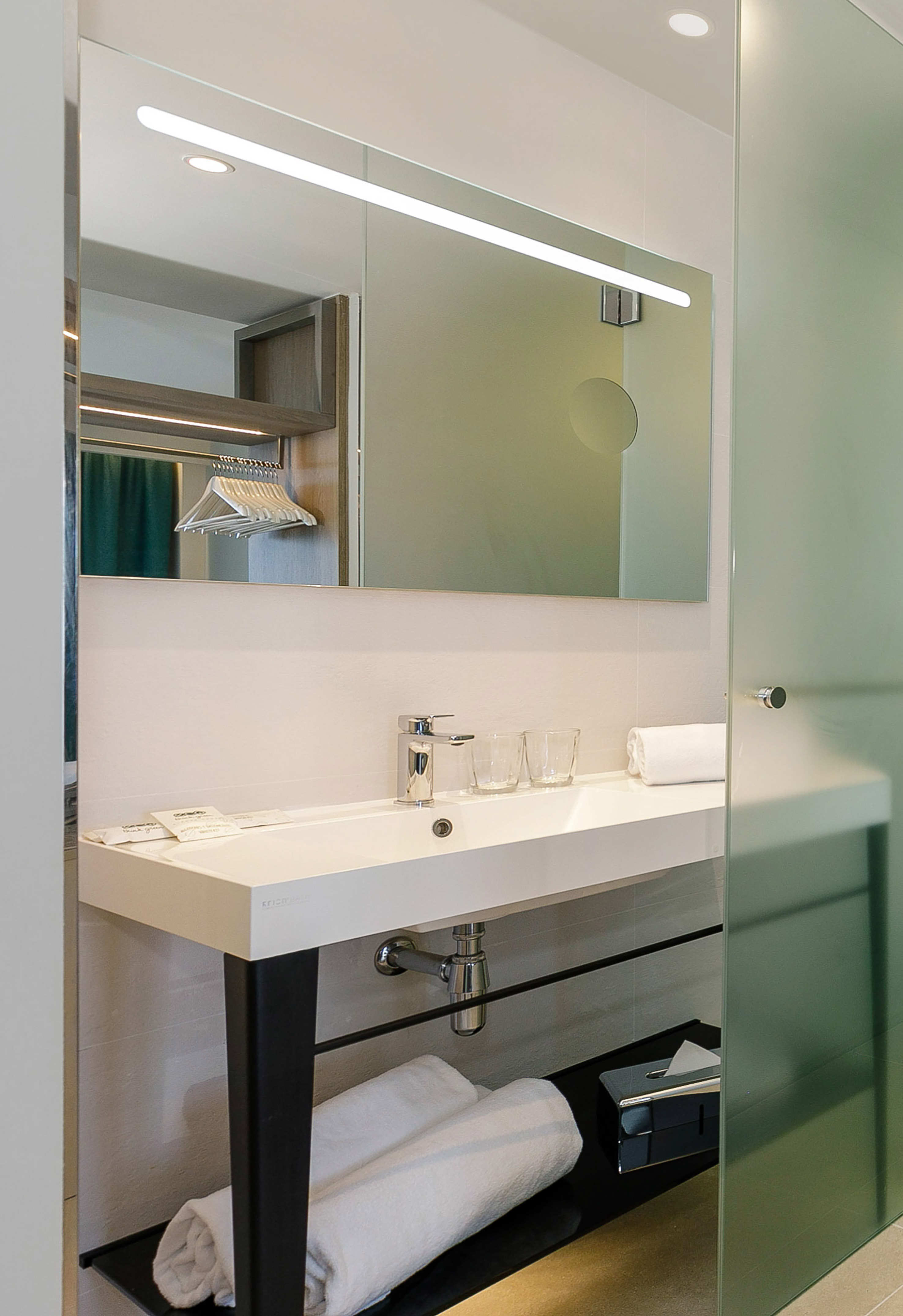 Modern hotel bathroom vanity with white sink, LED mirror, and glass shower.