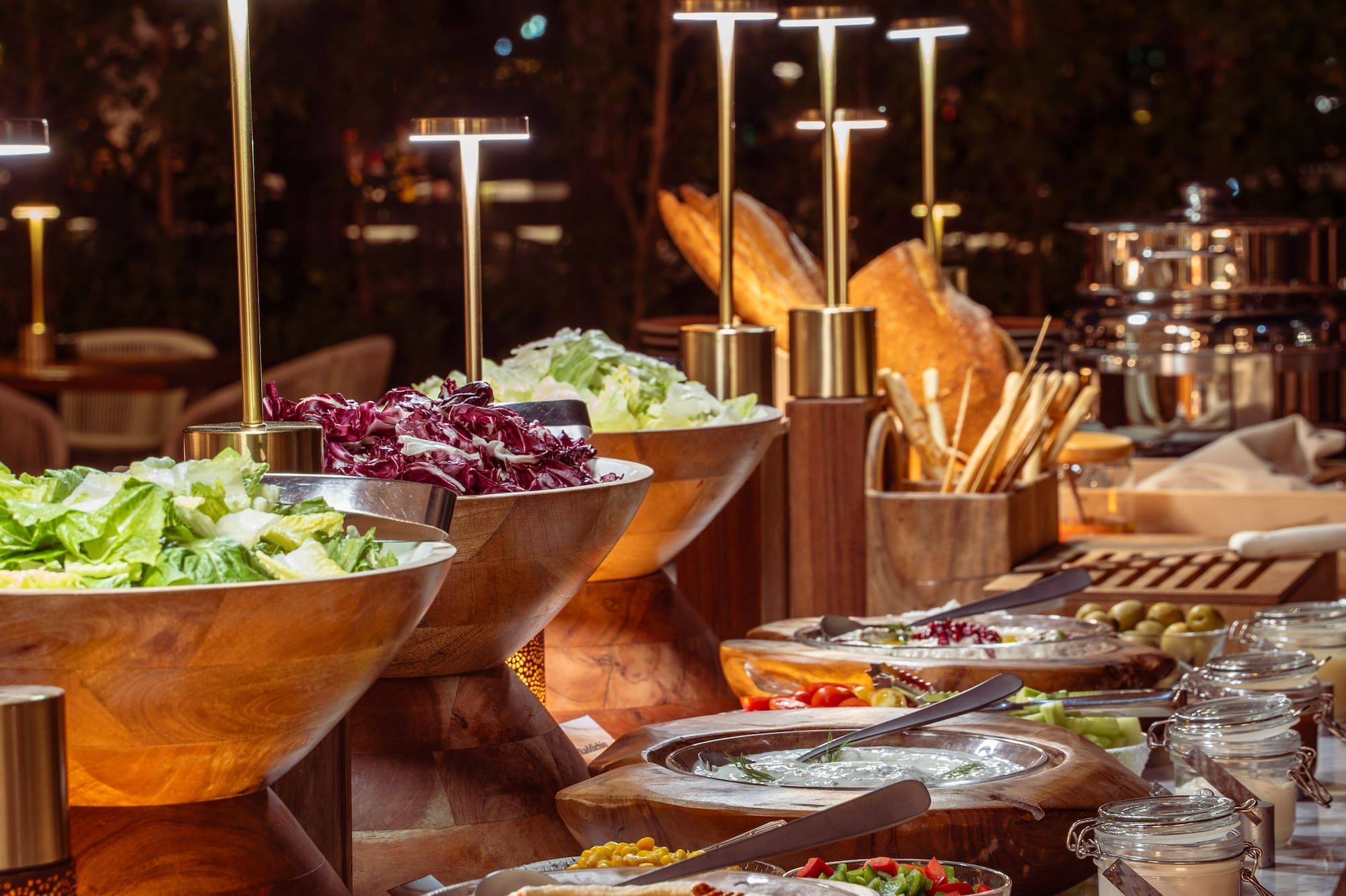 Elegant buffet with fresh salads, hummus, dips, and bread under warm lights.
