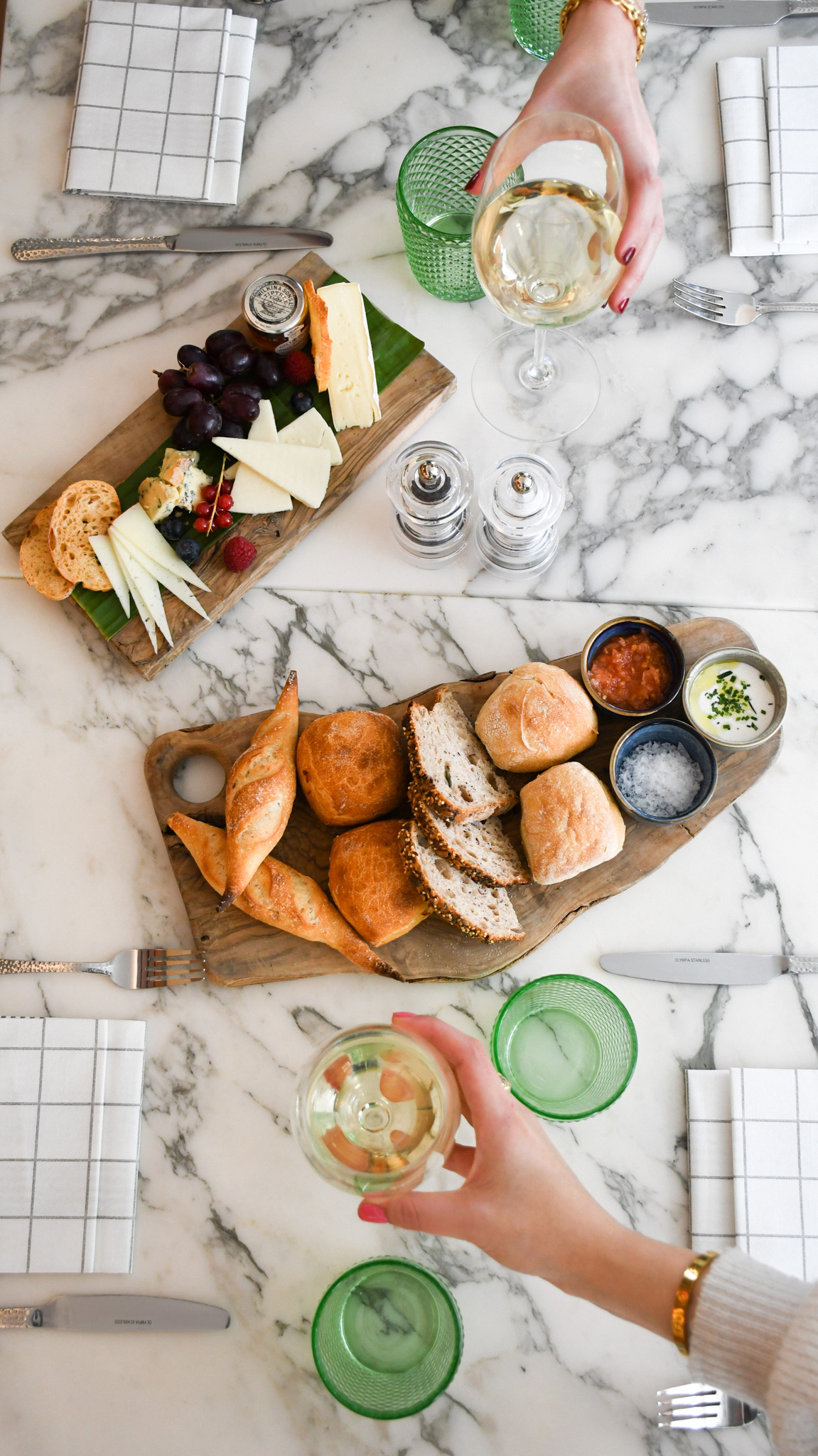 Charcuterie board with cheese, bread, dips, white wine on a marble table.