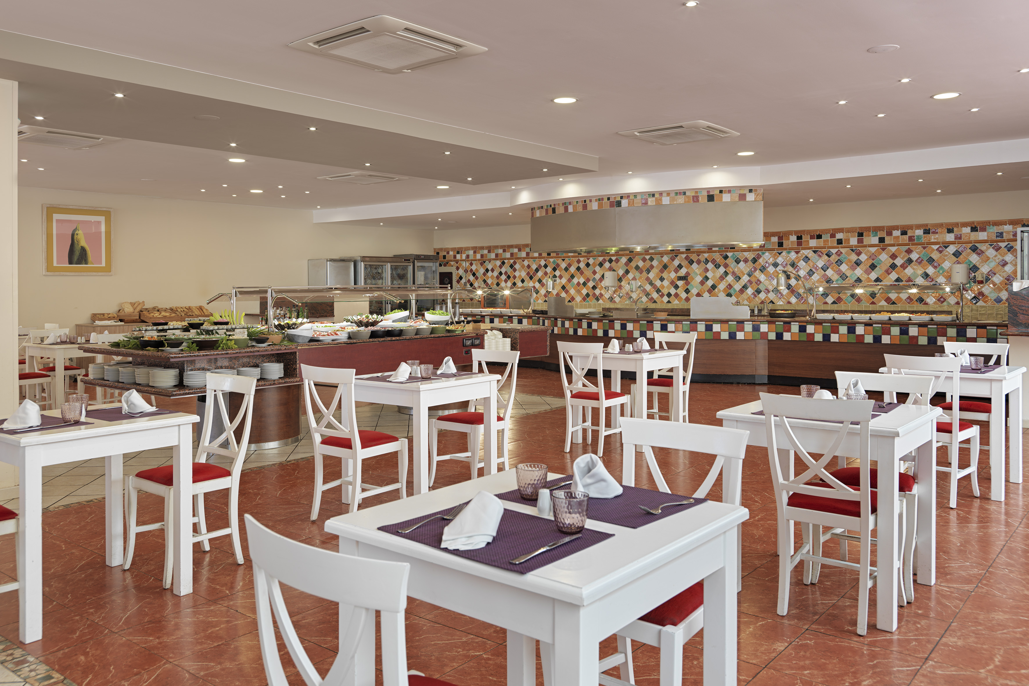 Hotel restaurant buffet with hot and cold food, white tables, red chairs.