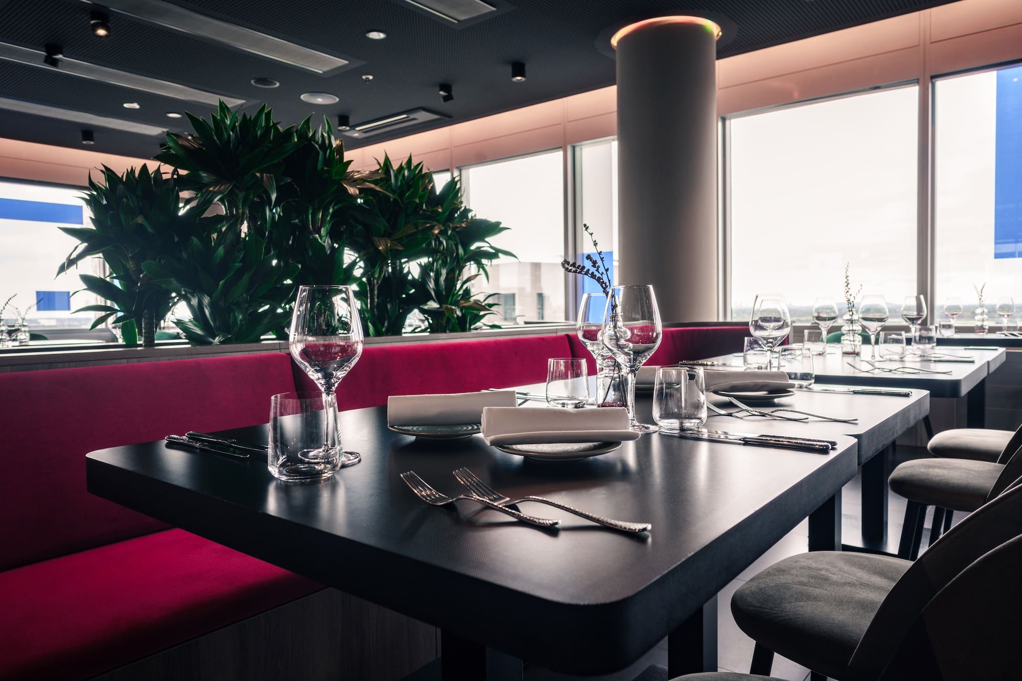 Modern restaurant dining with elegant set tables, red booth, and window view.