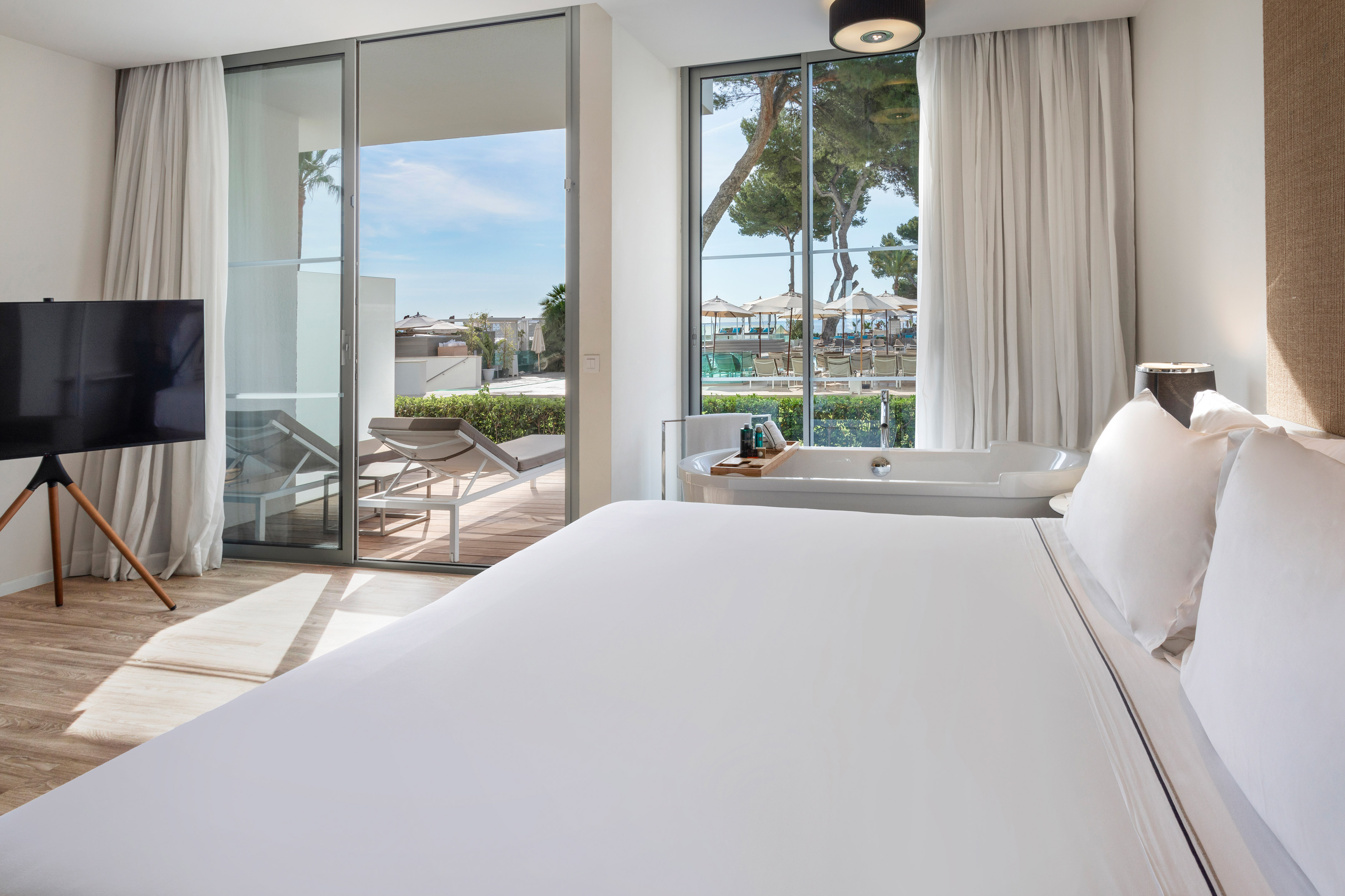 Sleek hotel room with bed, freestanding tub, balcony, and resort pool view.