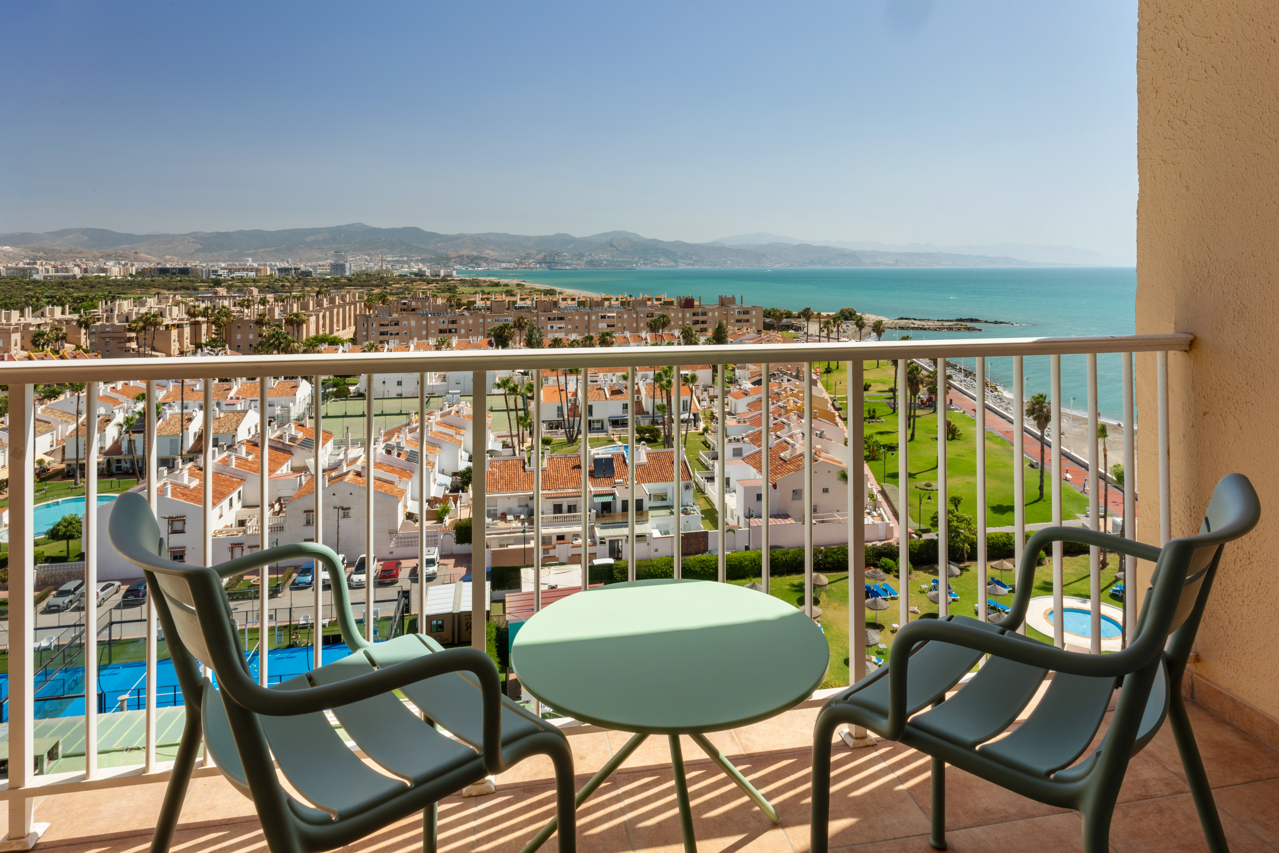 Balcón con vista al mar Mediterráneo, edificios y montañas bajo el sol.