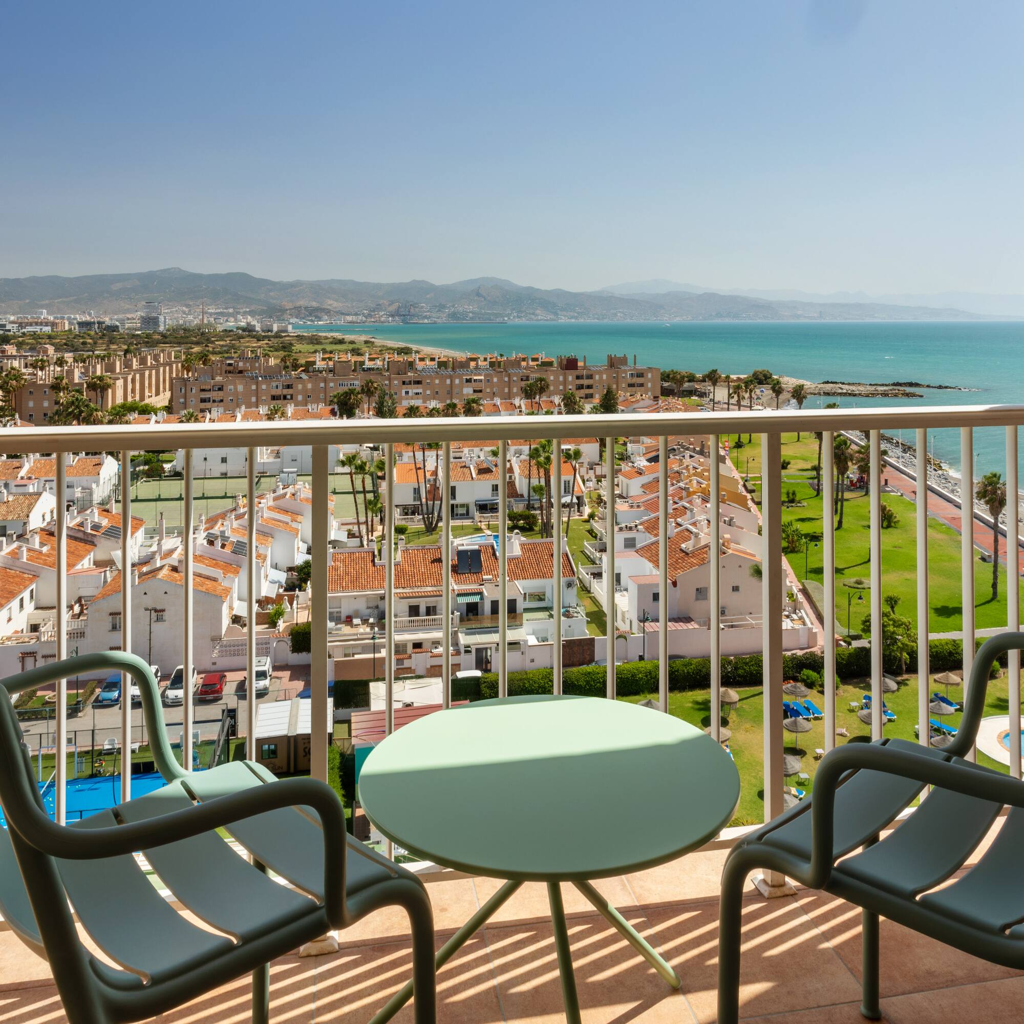 Balcón con vista al mar Mediterráneo, edificios y montañas bajo el sol.