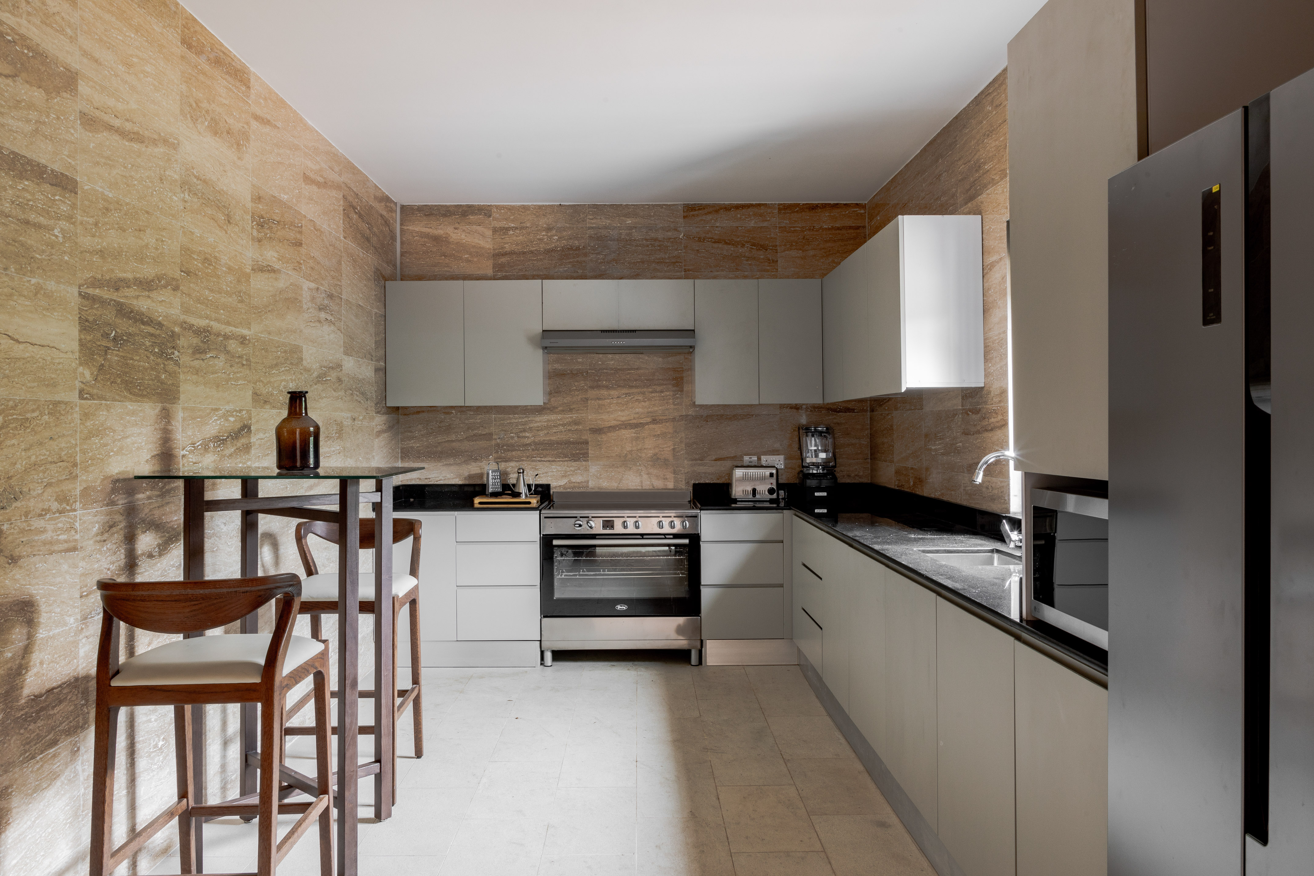 Modern kitchen with stone tile walls, grey cabinets, stainless appliances, bar.