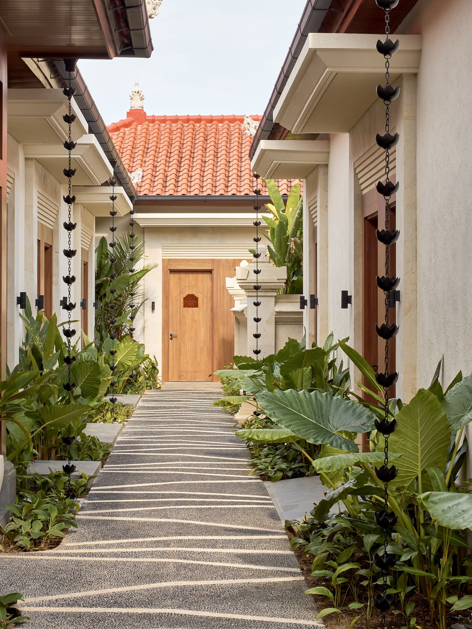 Balinese resort pathway with lush tropical plants and decorative lotus rain chains.
