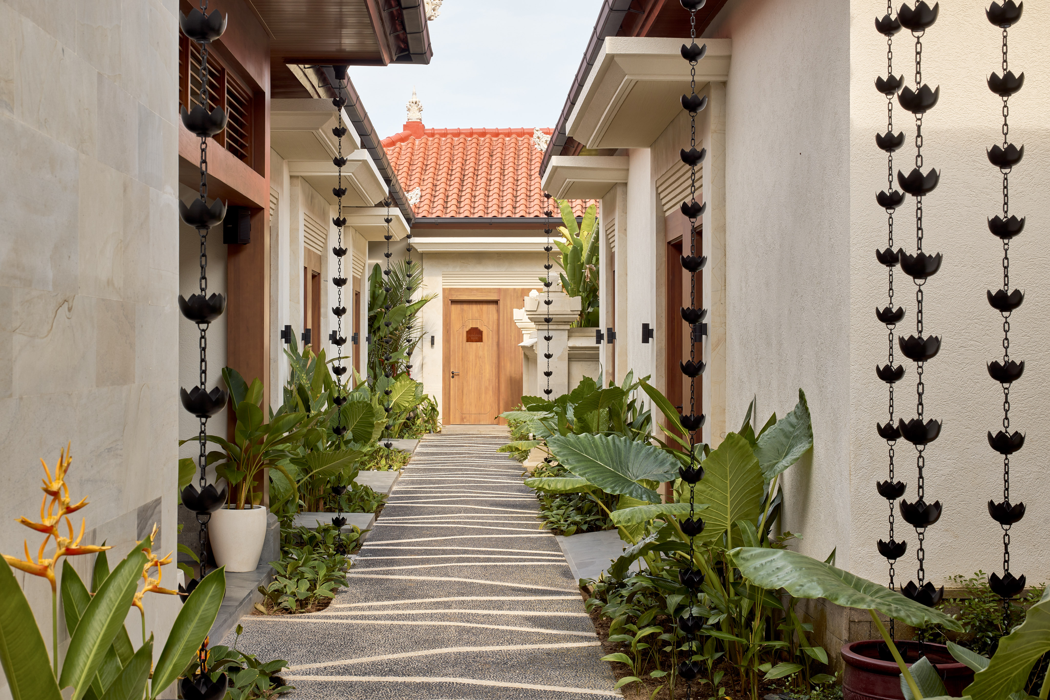 Balinese resort pathway with lush tropical plants and decorative lotus rain chains.