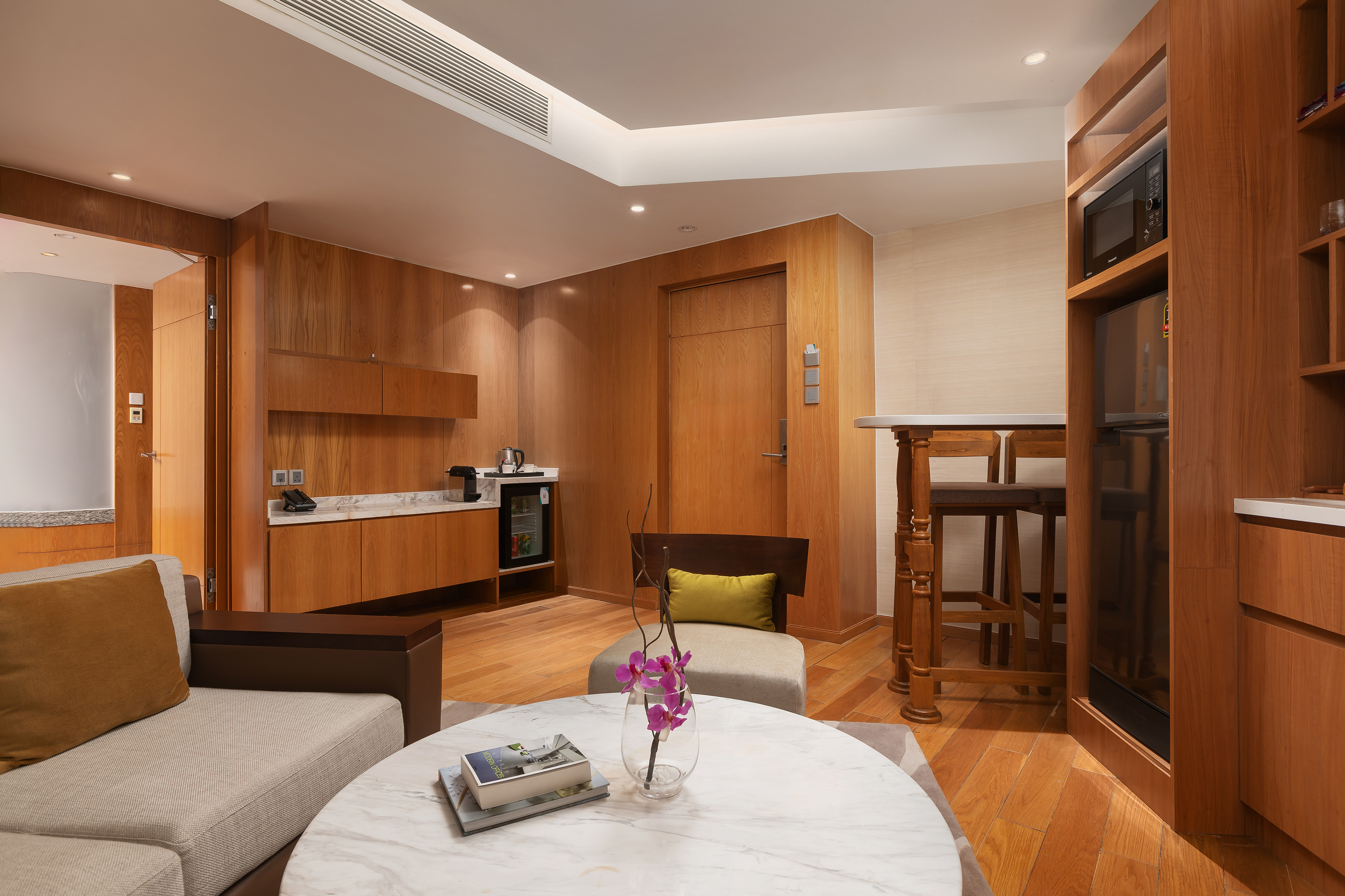 Modern hotel suite living area and kitchenette with wood interior, marble accents.