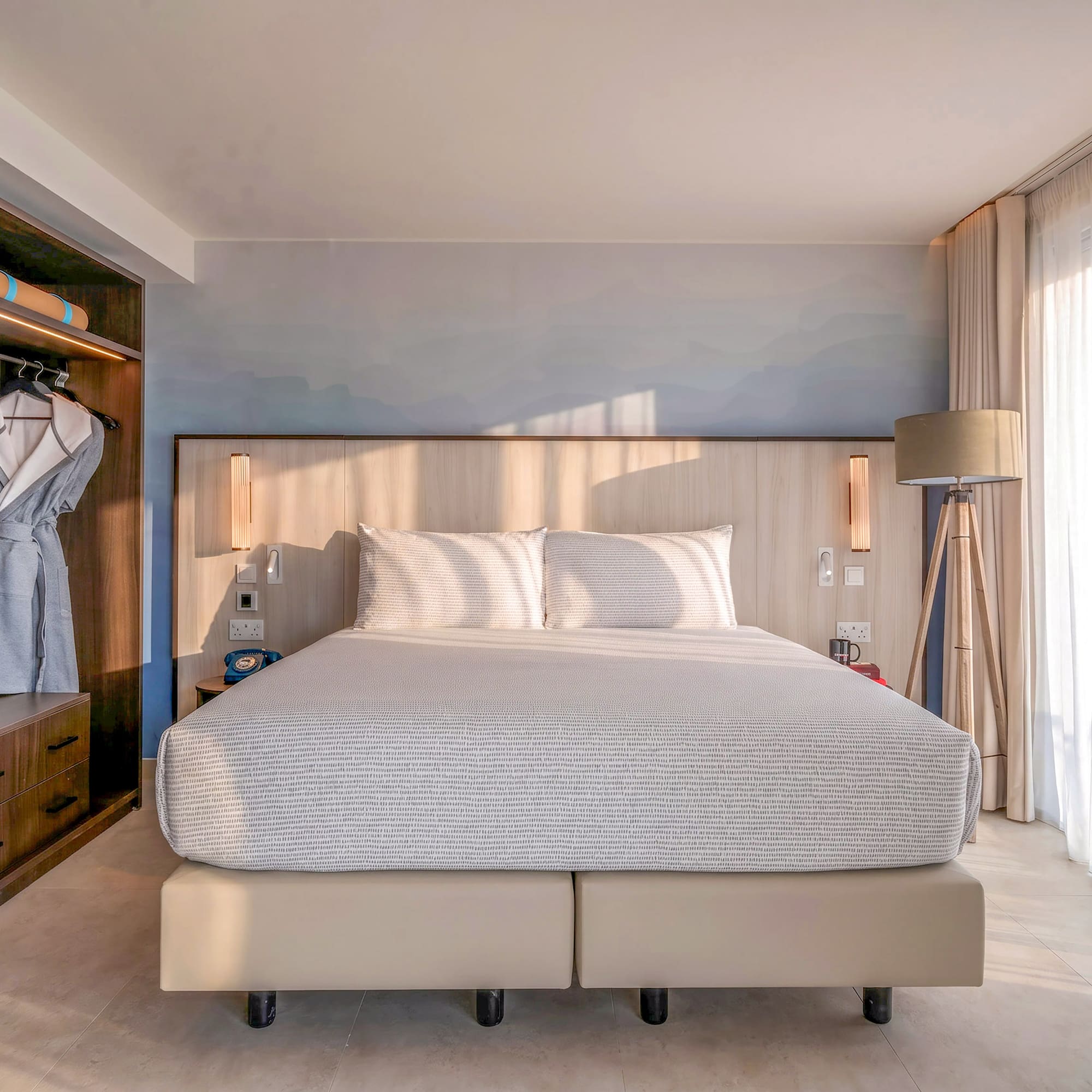 Bright hotel room with king bed, built-in storage, and sheer curtains.
