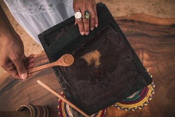 a person holding a spoon over a black square with brown powder