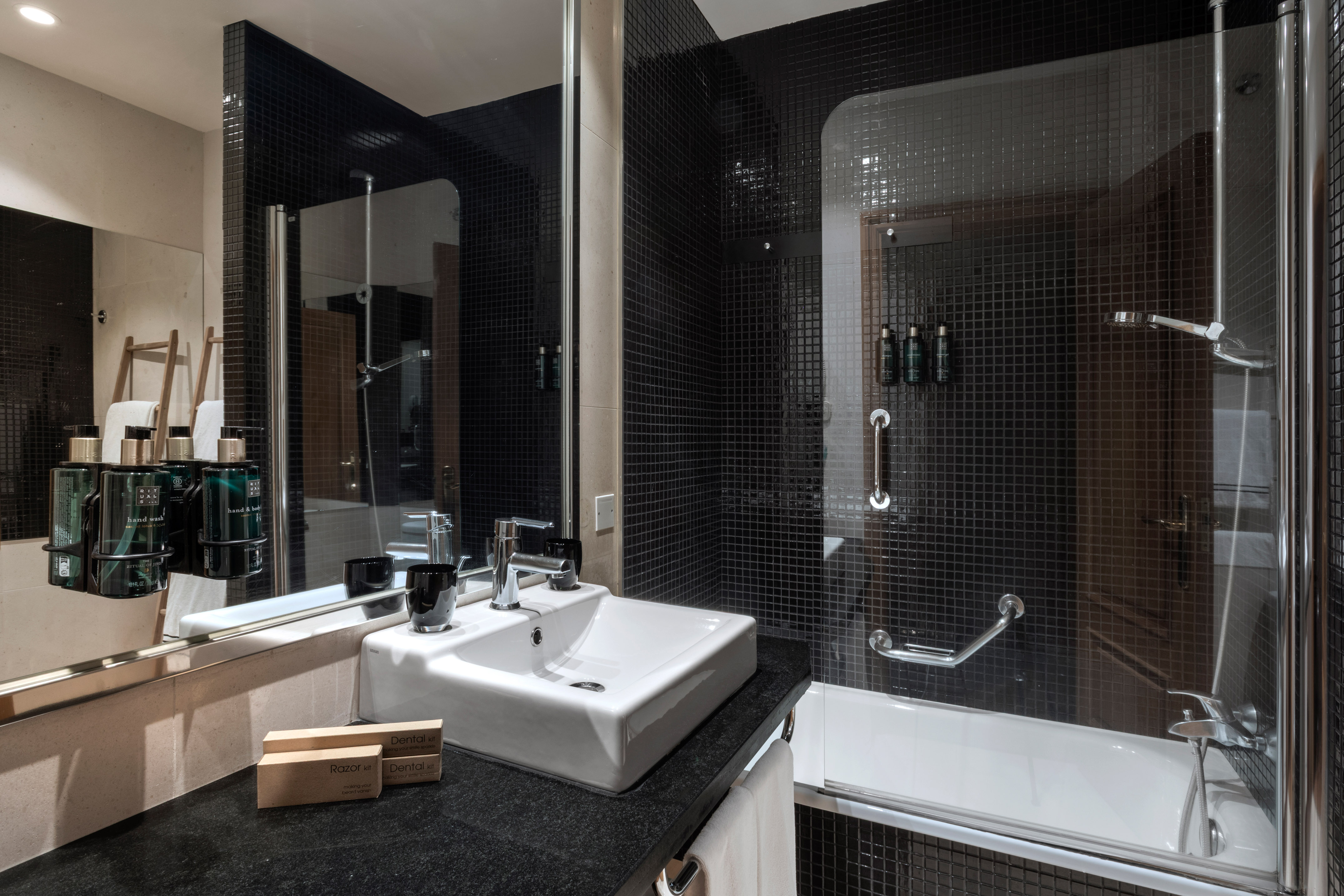 Sleek black mosaic tiled bathroom with white sink, mirror, shower-tub.