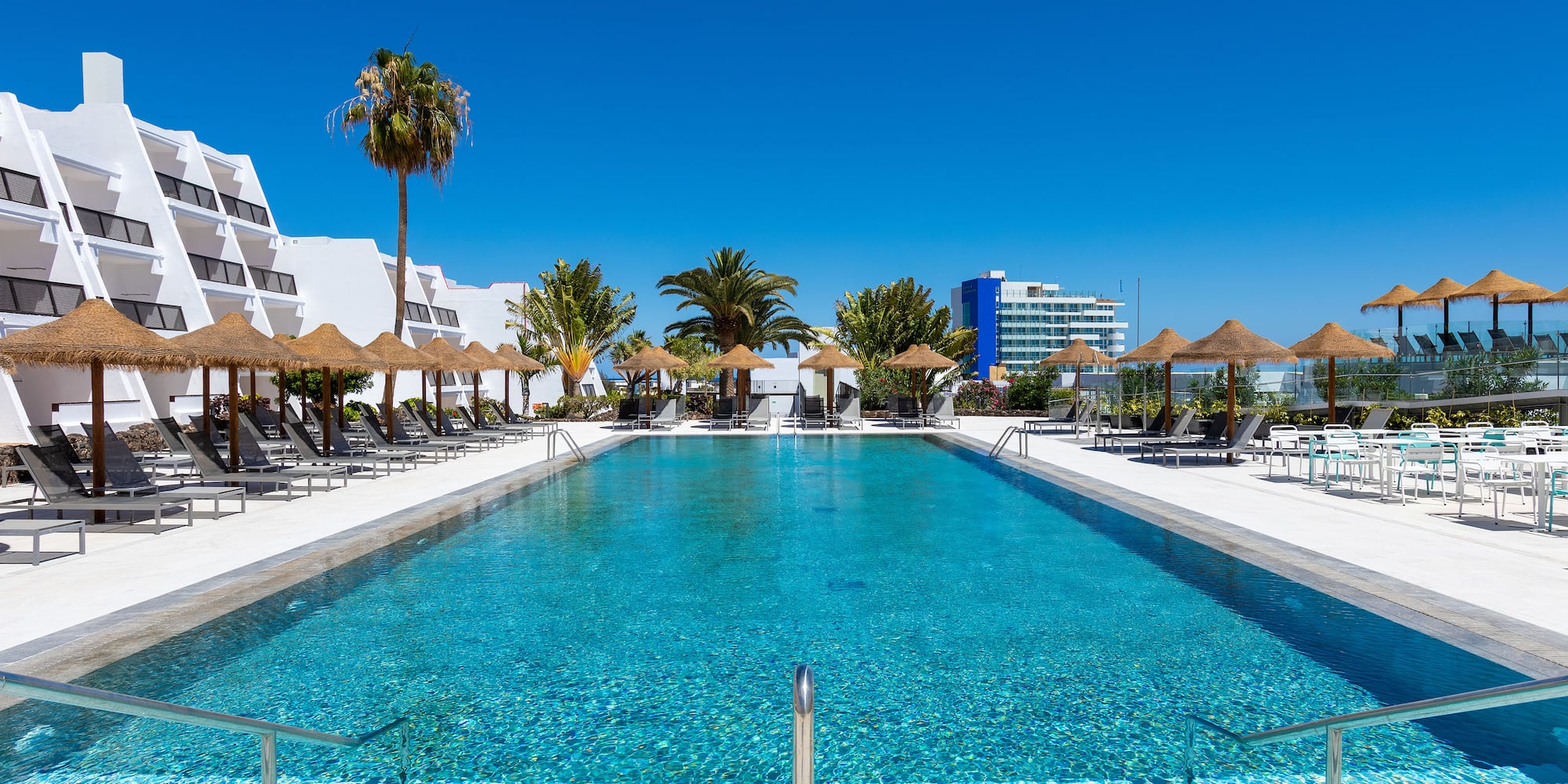 a swimming pool with straw umbrellas and palm trees