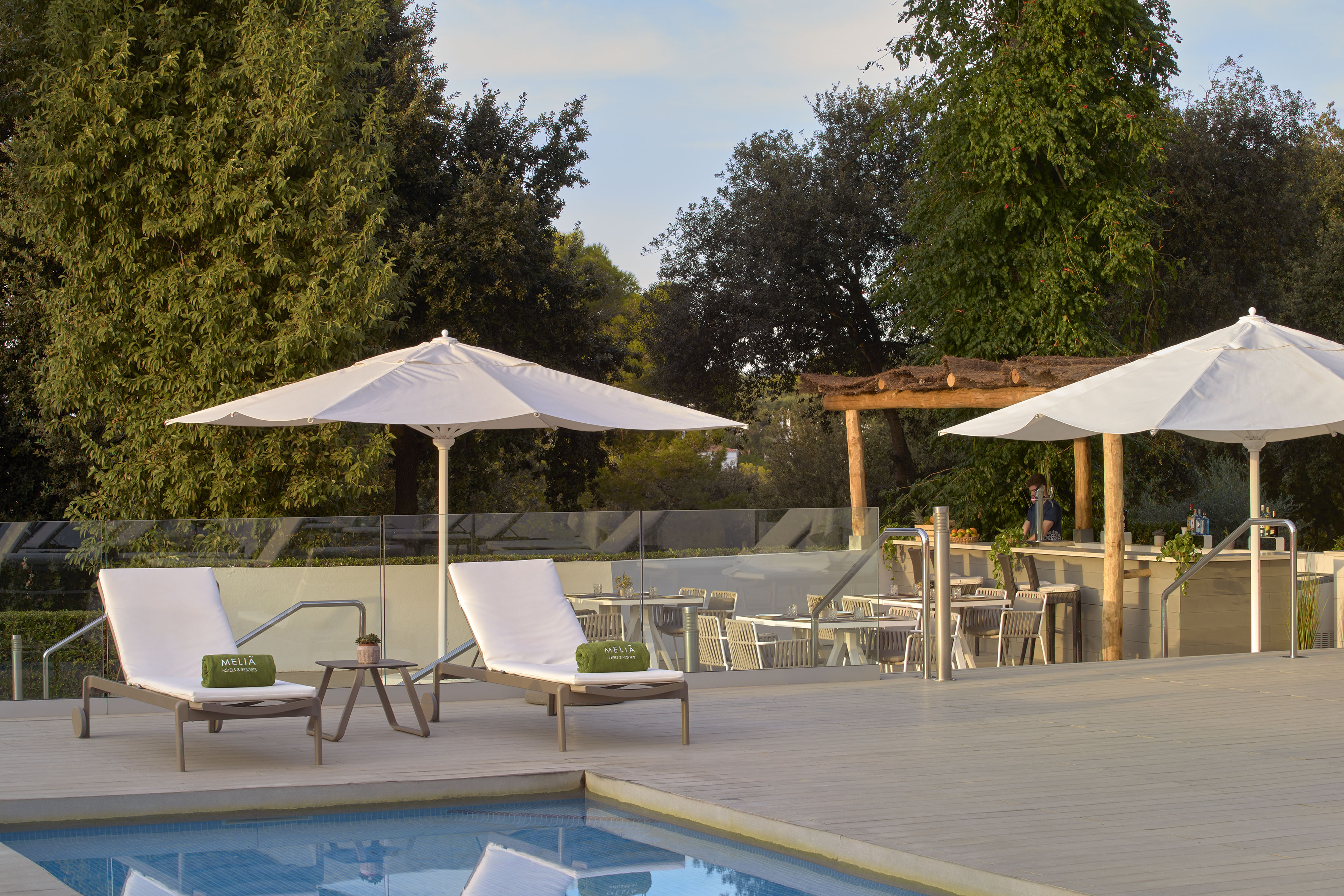 Meliá resort pool deck: lounge chairs, white umbrellas, outdoor bar, green trees.