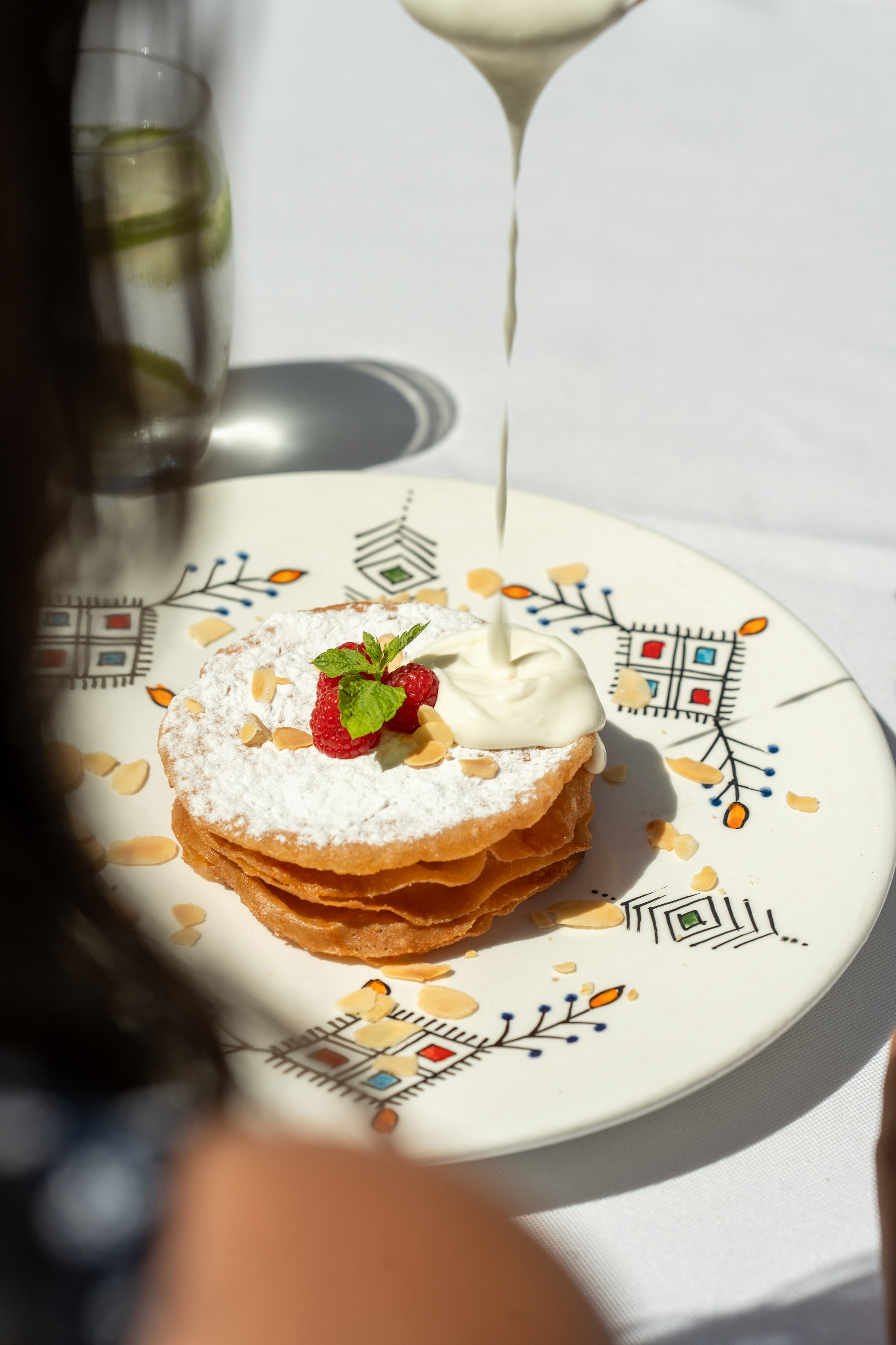 Cream pouring on stacked pancakes with raspberries, powdered sugar, and almonds. - Restaurant Darna, Showkochen - SOL Oasis Marrakech, Marrakesch