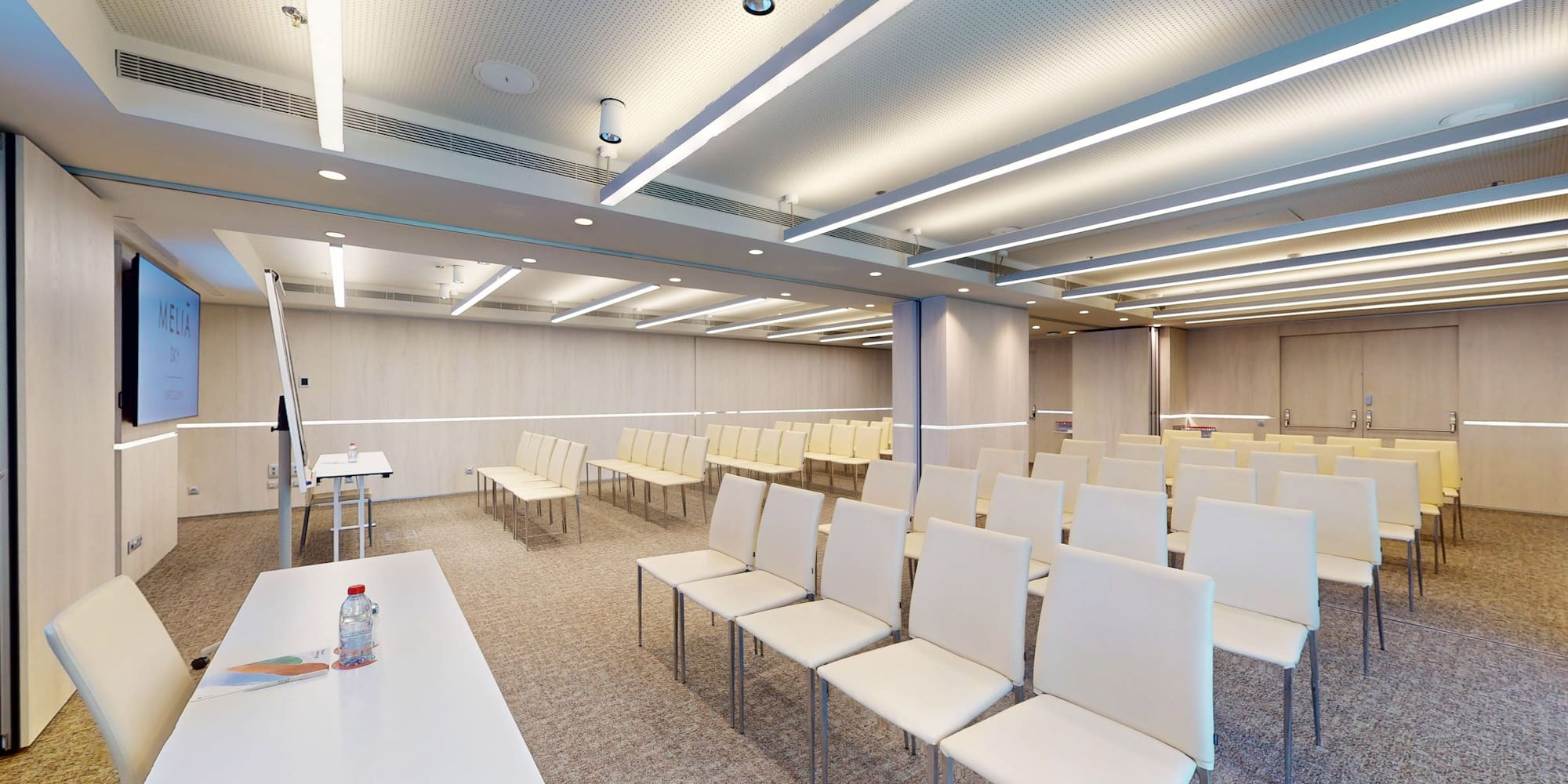 Modern Meliá meeting room with rows of white chairs, screen, and presentation setup.