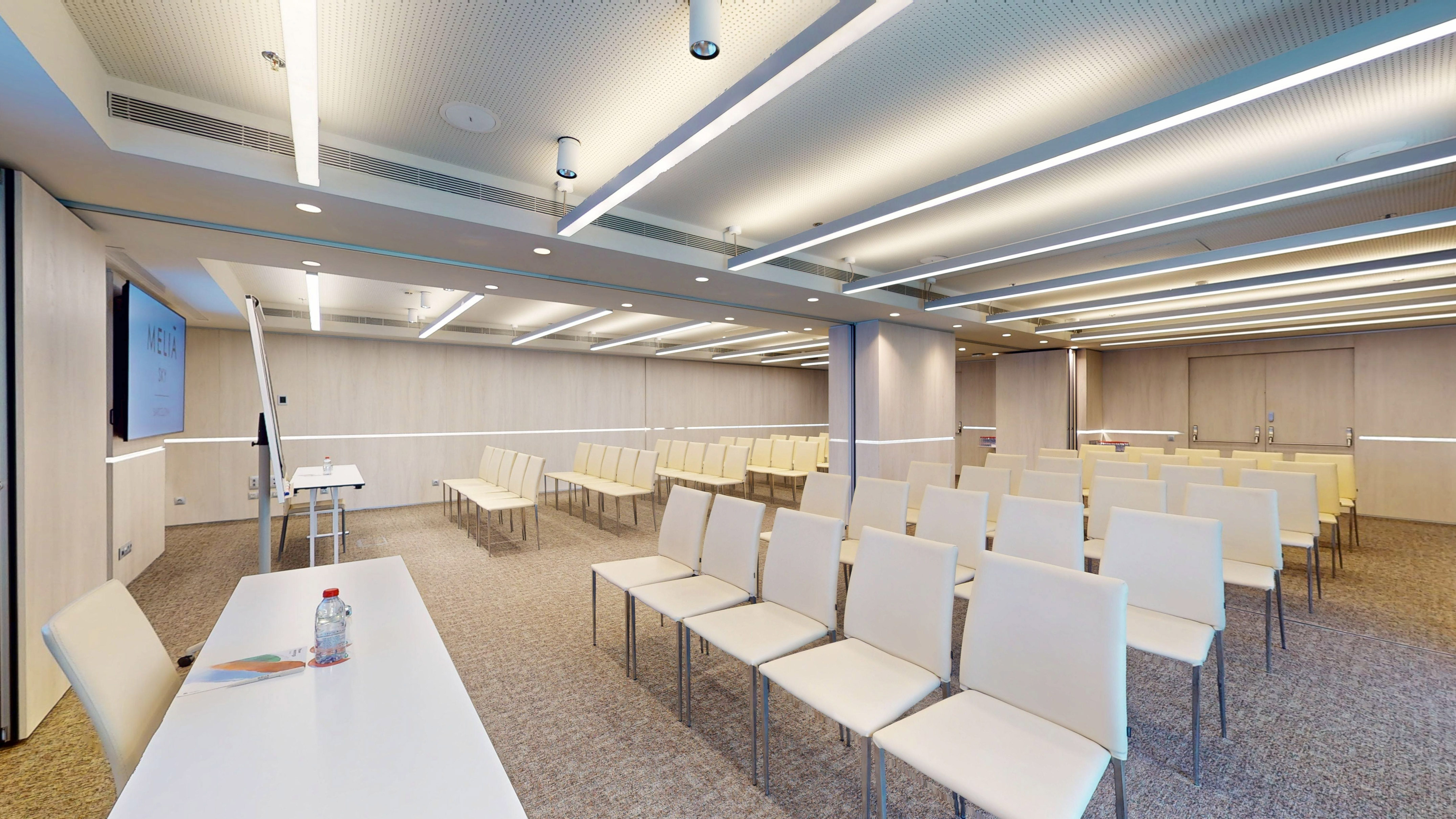 Modern Meliá meeting room with rows of white chairs, screen, and presentation setup.