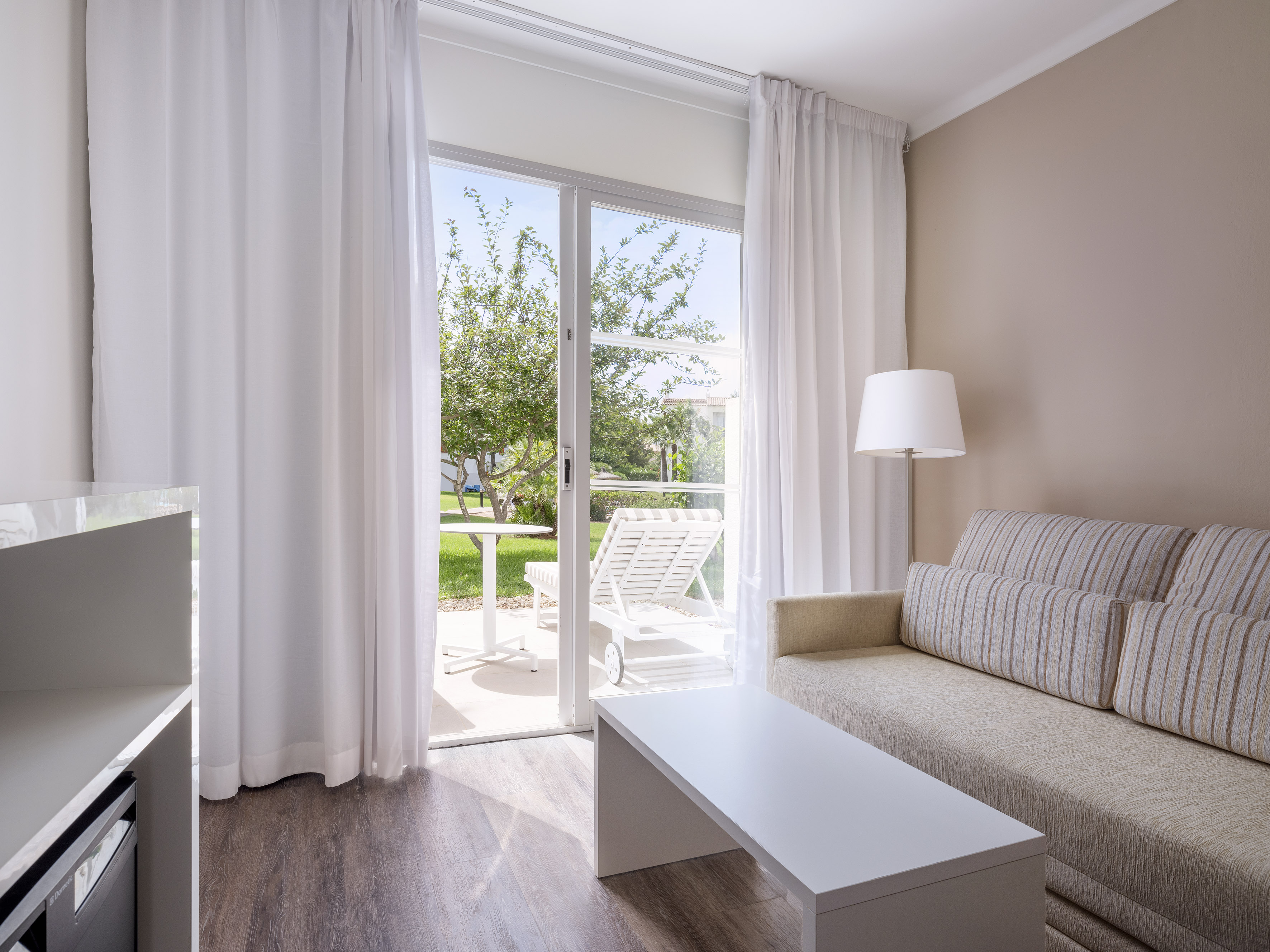 Bright hotel suite living room, sofa, coffee table, garden patio access.