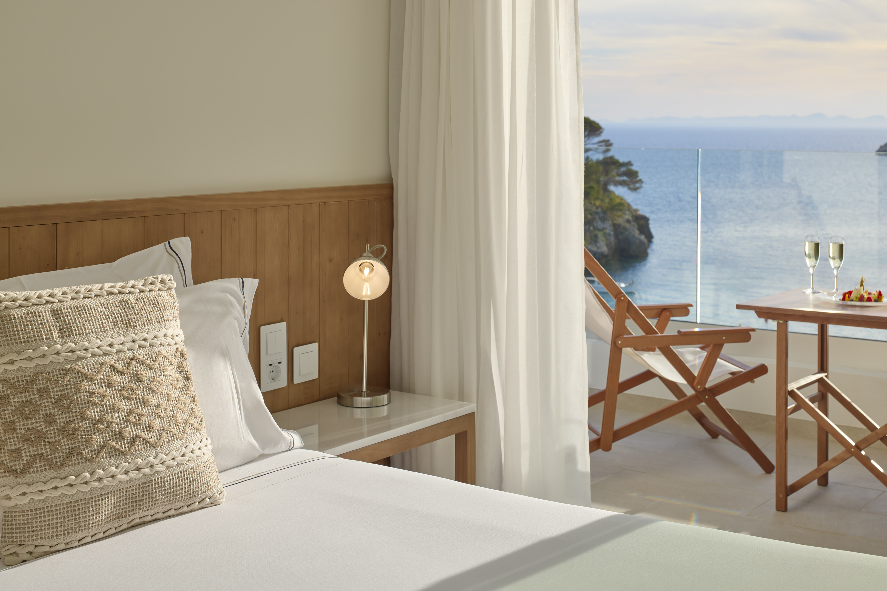 Hotel bedroom with ocean view balcony, champagne, and fruit plate.