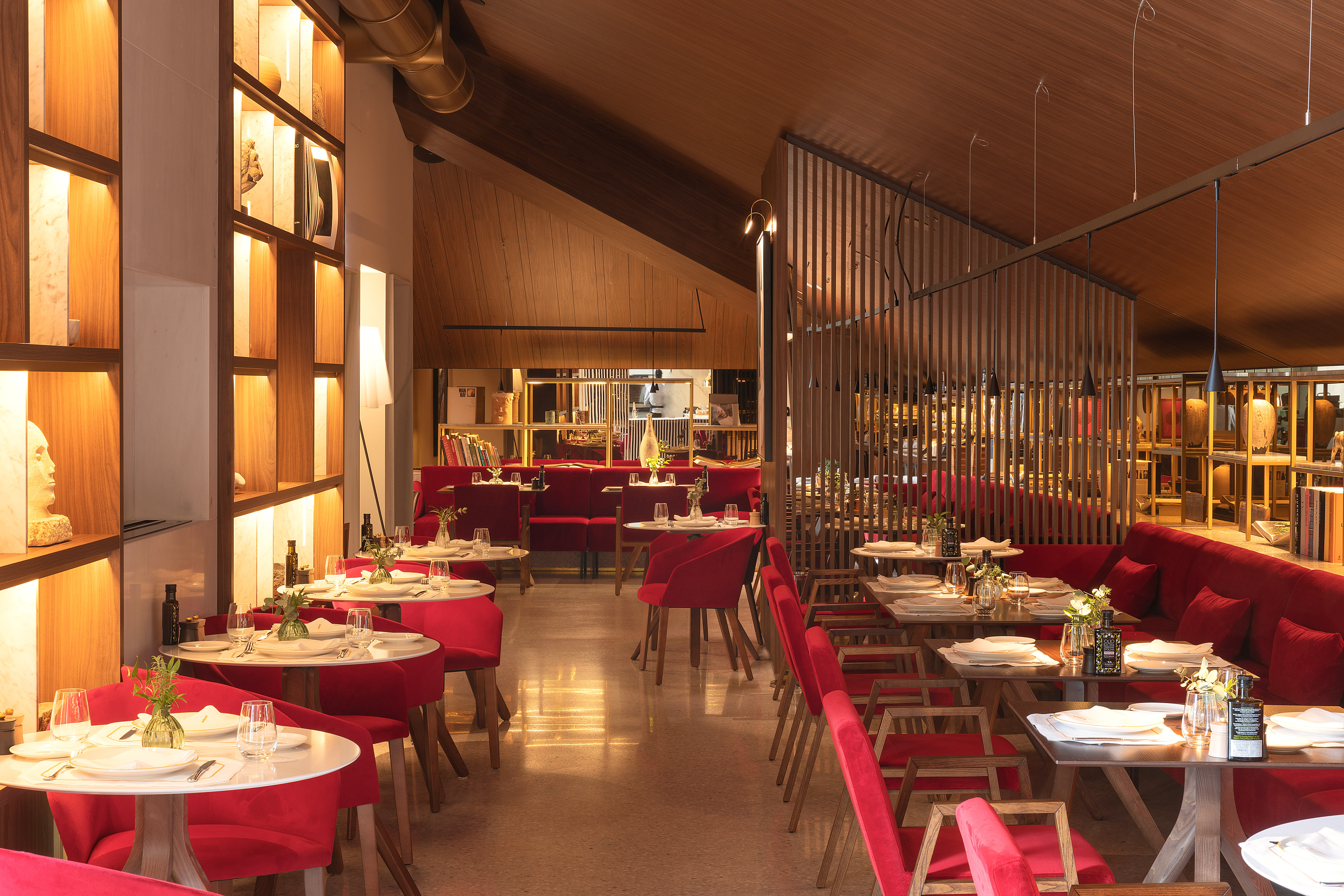 Contemporary restaurant dining room with red seating, warm lighting, and wood accents.
