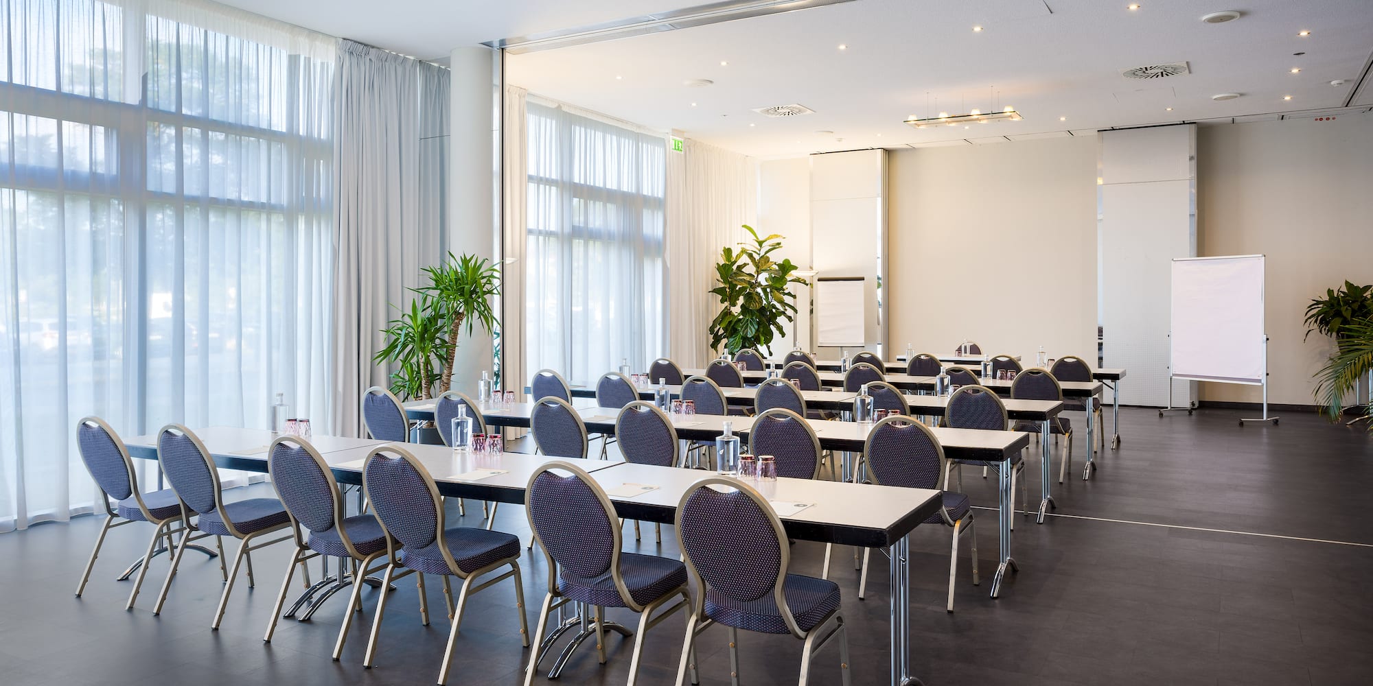 Conference room with classroom seating, tables, chairs, large windows, and whiteboard.
