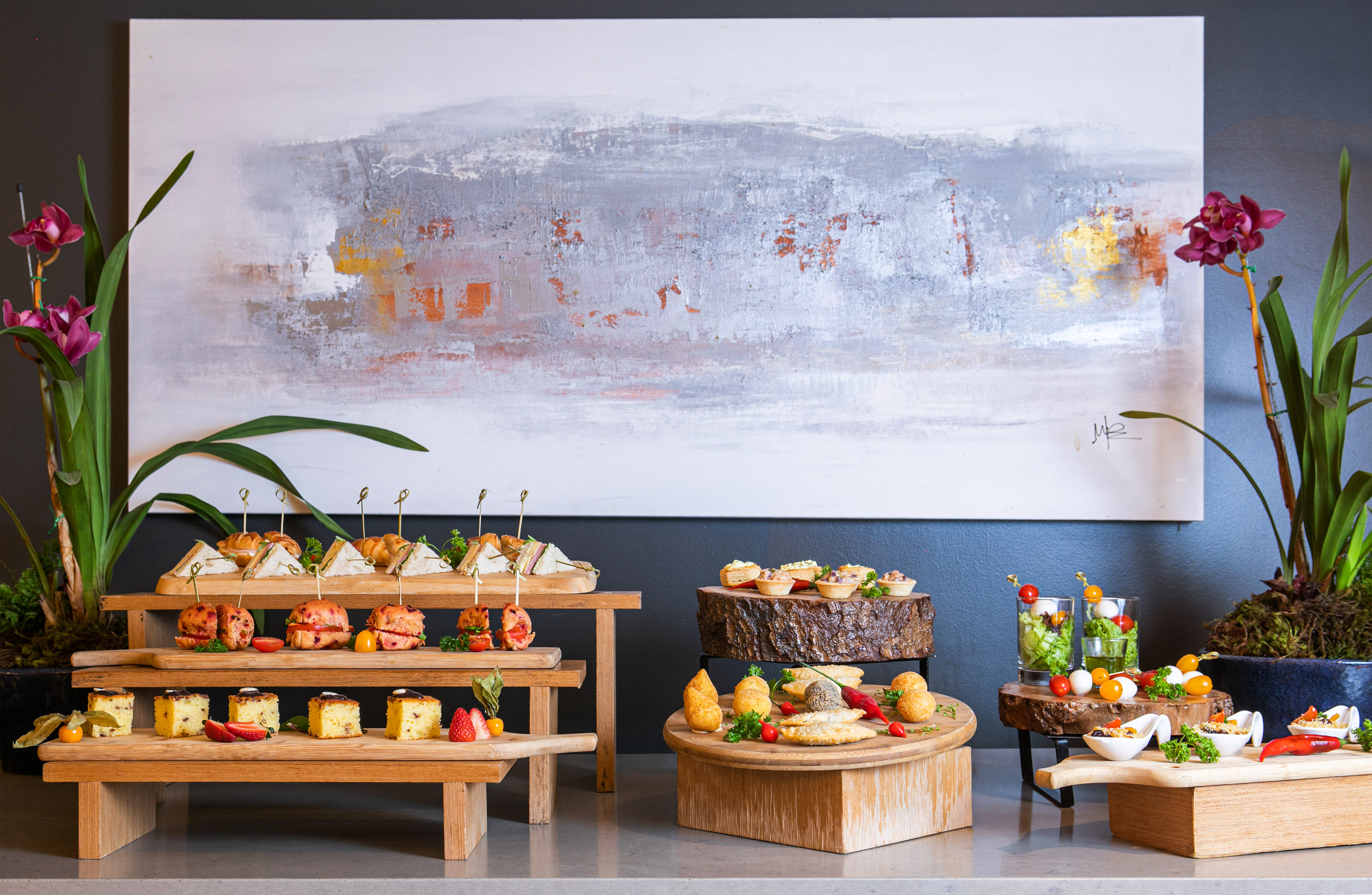 Buffet of gourmet appetizers, desserts, and small bites on wooden stands.