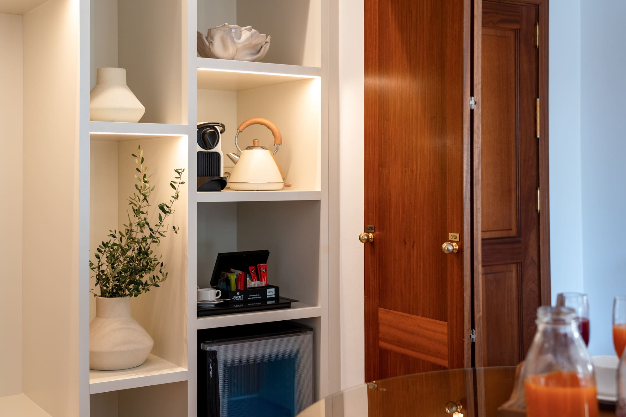 a white shelves with a tea kettle and a plant in a room