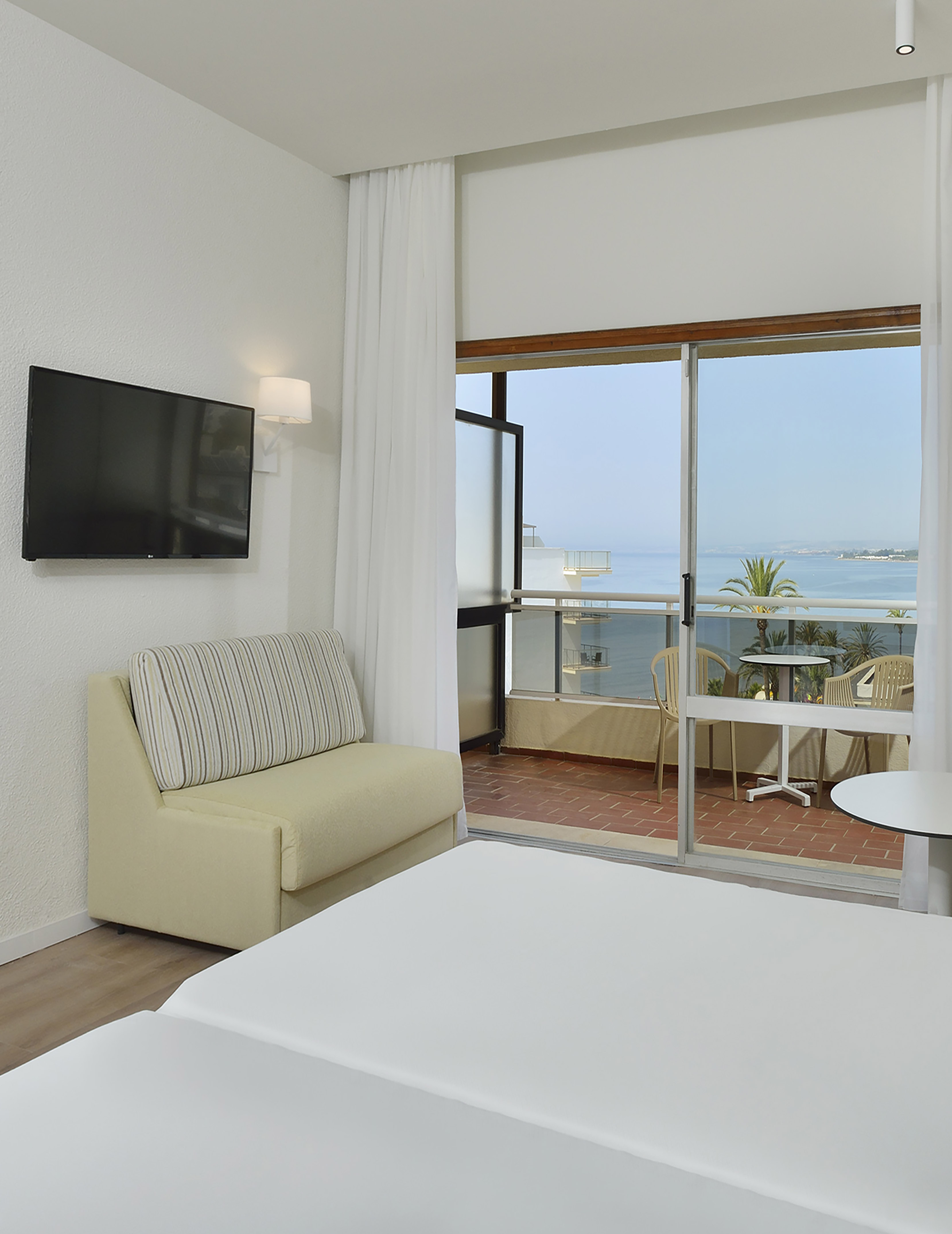 Modern hotel room, ocean view balcony, TV, sofa. Coastal stay.