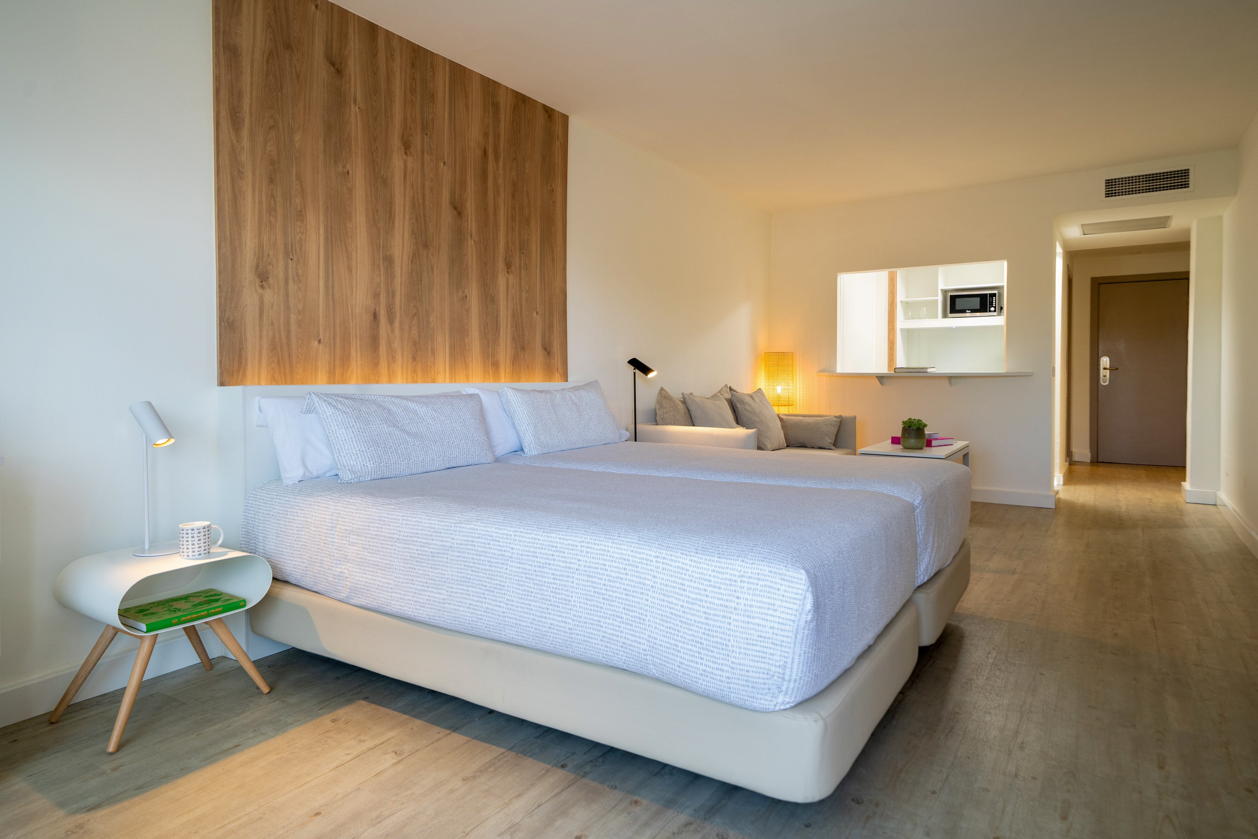 Modern hotel room with bed, wood paneling, sofa, and kitchenette.