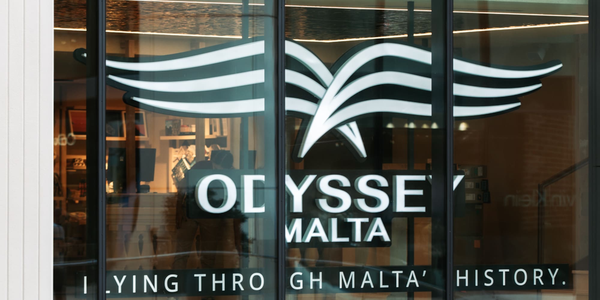 Odyssey Malta logo on glass building facade, with Amorino Gelato below.