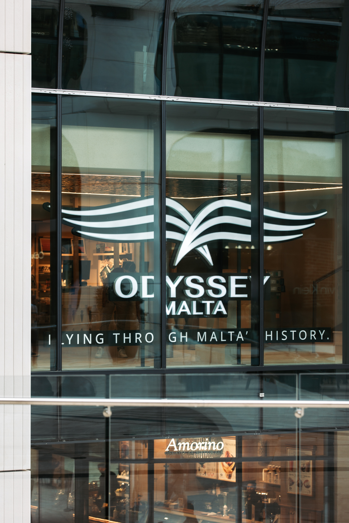Odyssey Malta logo on glass building facade, with Amorino Gelato below.