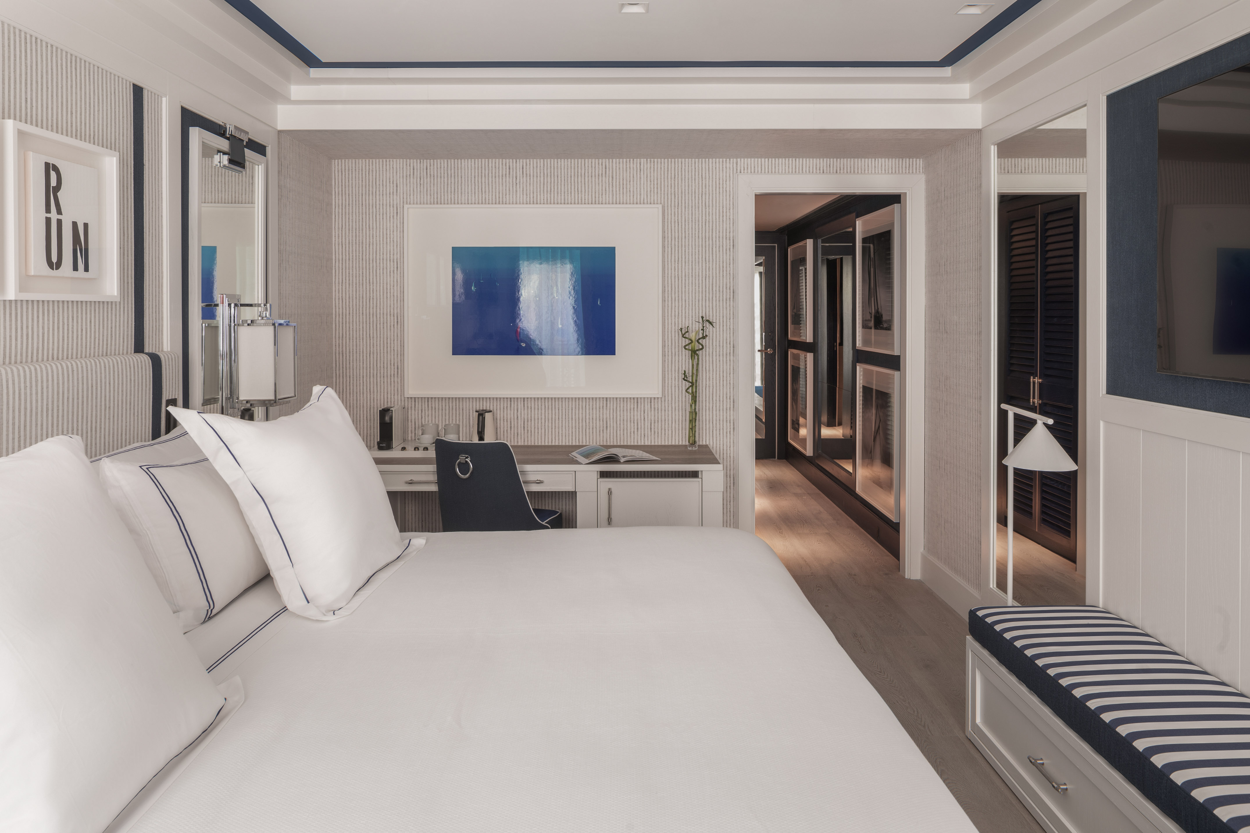 Modern luxury hotel room with king bed, nautical decor, desk, and abstract art.
