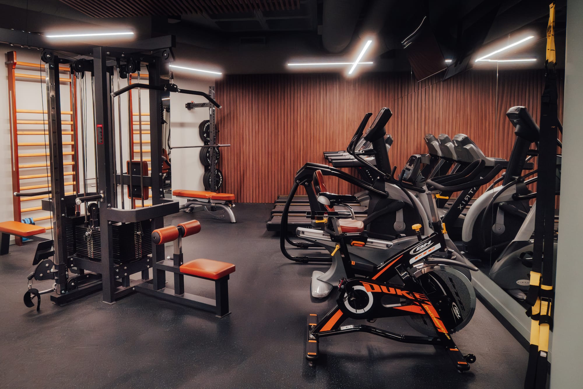 Modern gym with cable machine, spin bike, treadmills, and weight benches.
