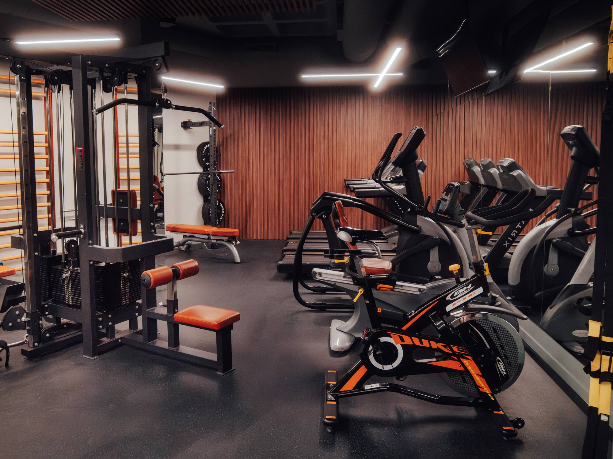 Modern gym with cable machine, spin bike, treadmills, and weight benches.