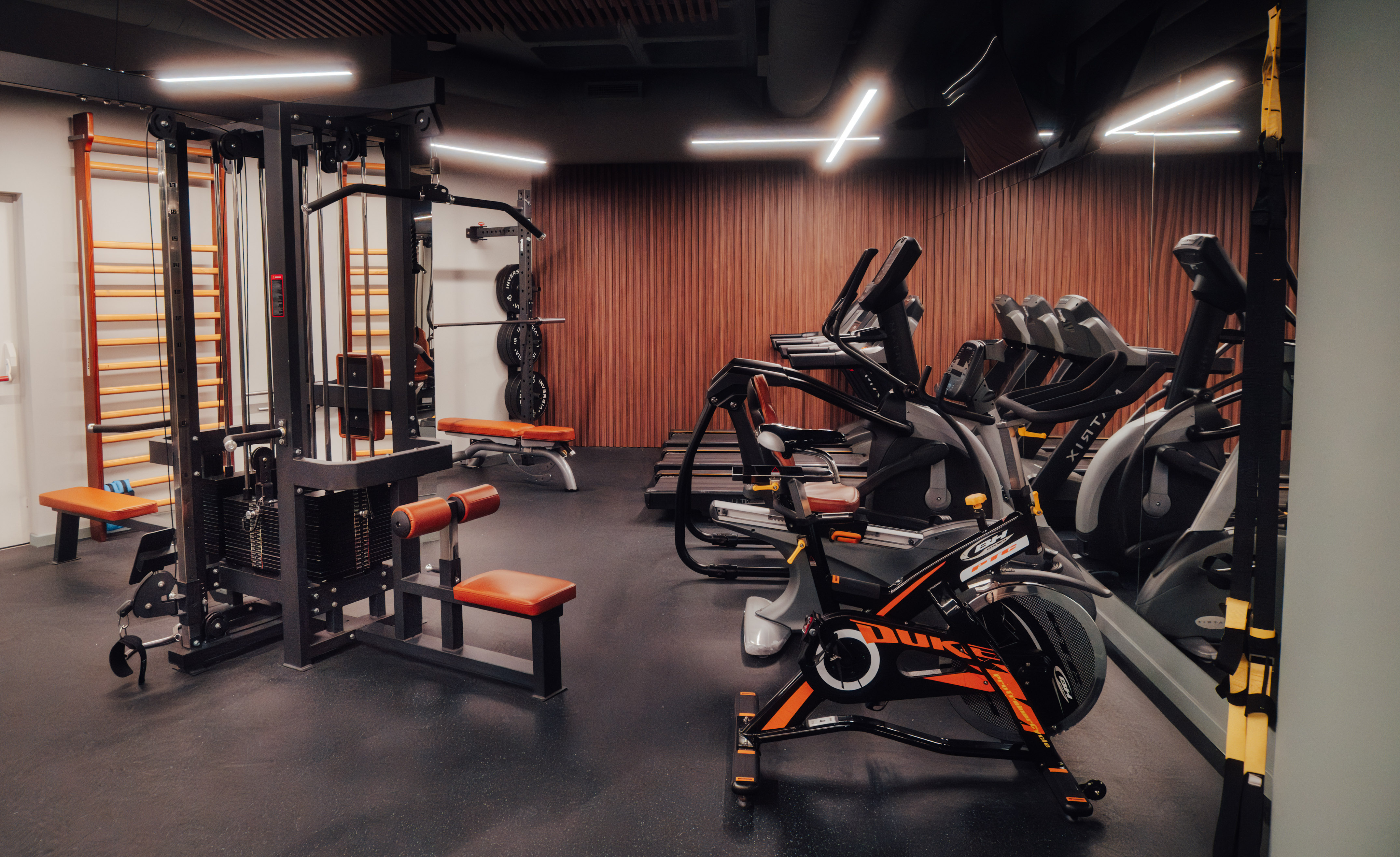 Modern gym with cable machine, spin bike, treadmills, and weight benches.