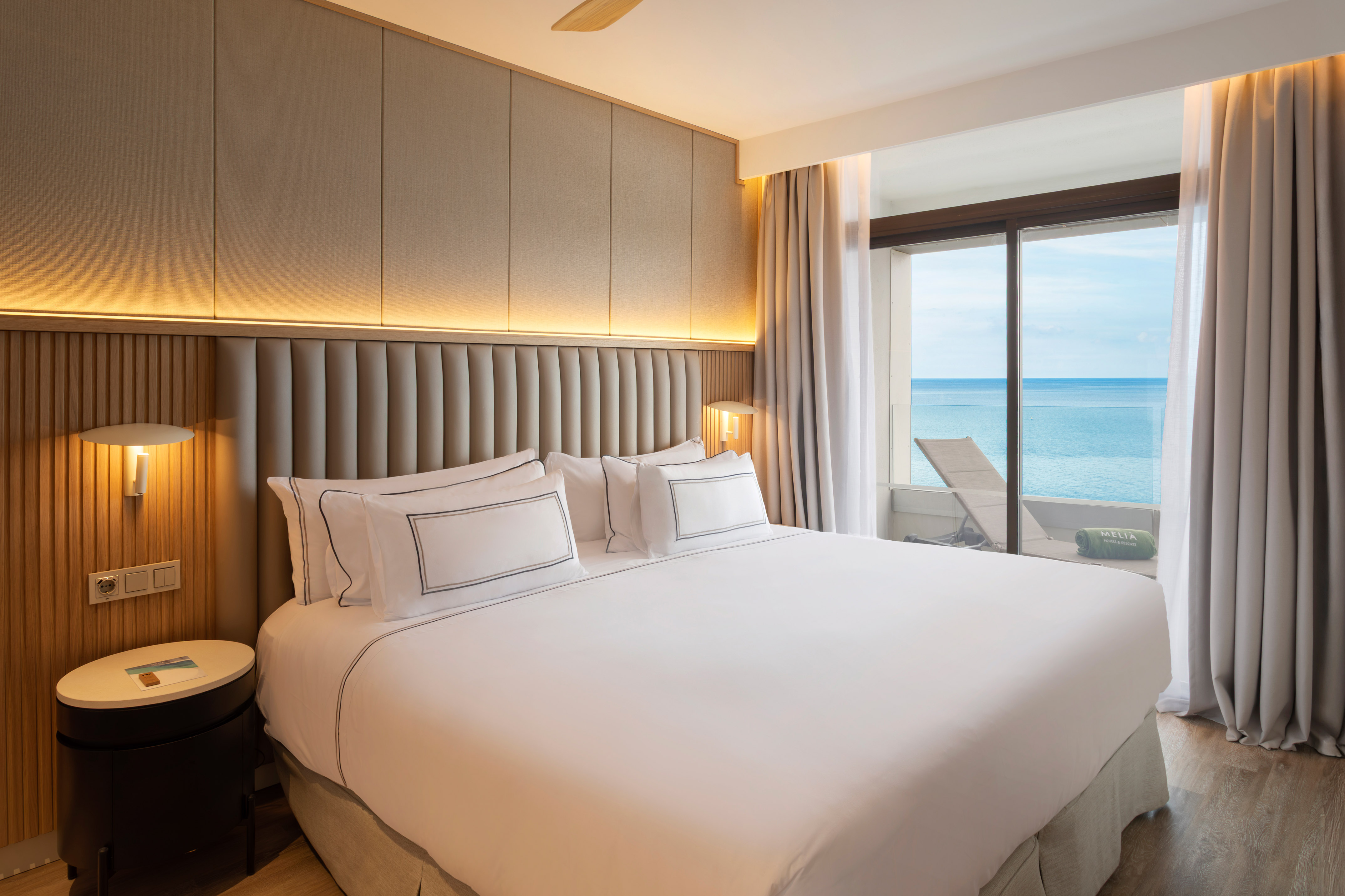 Modern hotel room with king bed and ocean view balcony.
