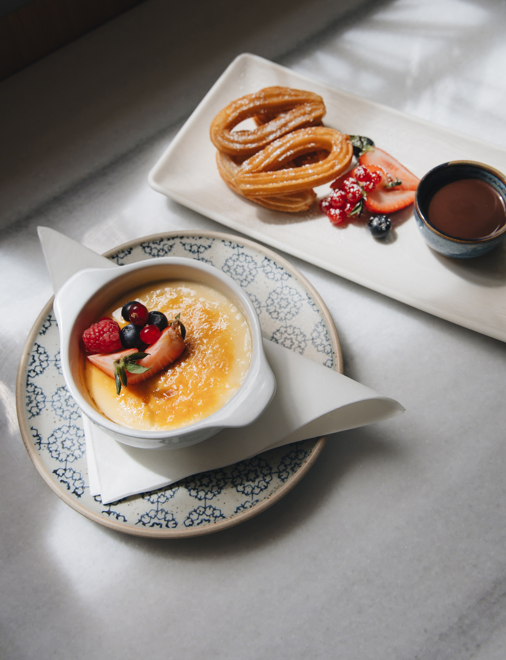 Crème brûlée with berries, churros with chocolate dip on marble.