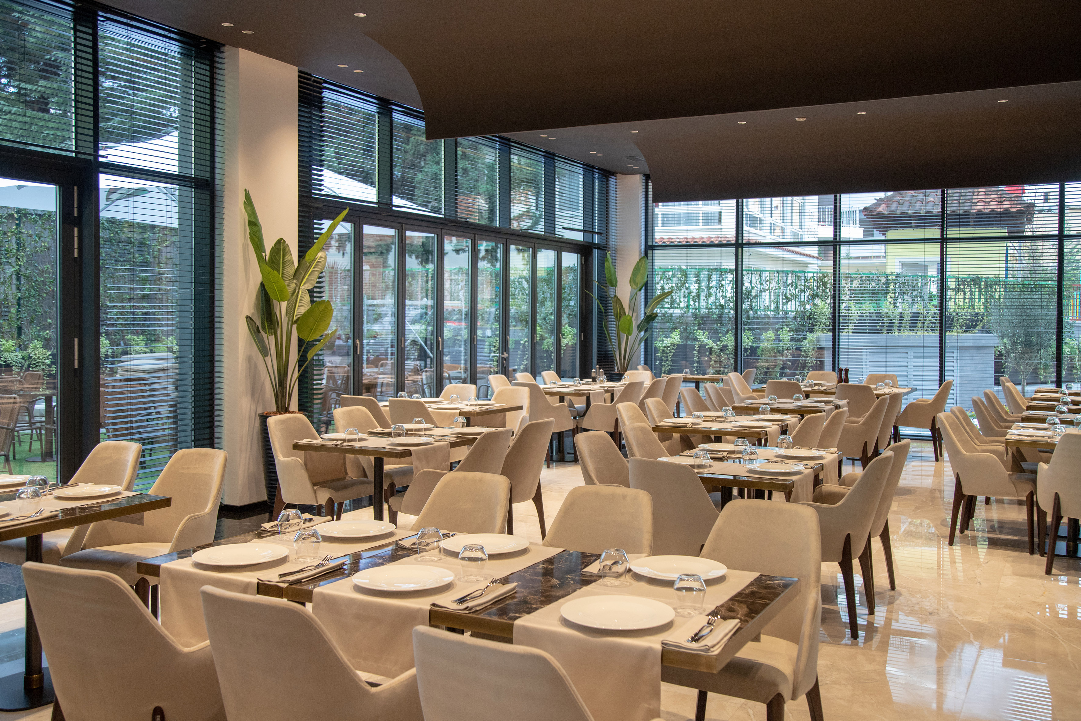 Modern restaurant interior with set tables, cream chairs, and large windows.