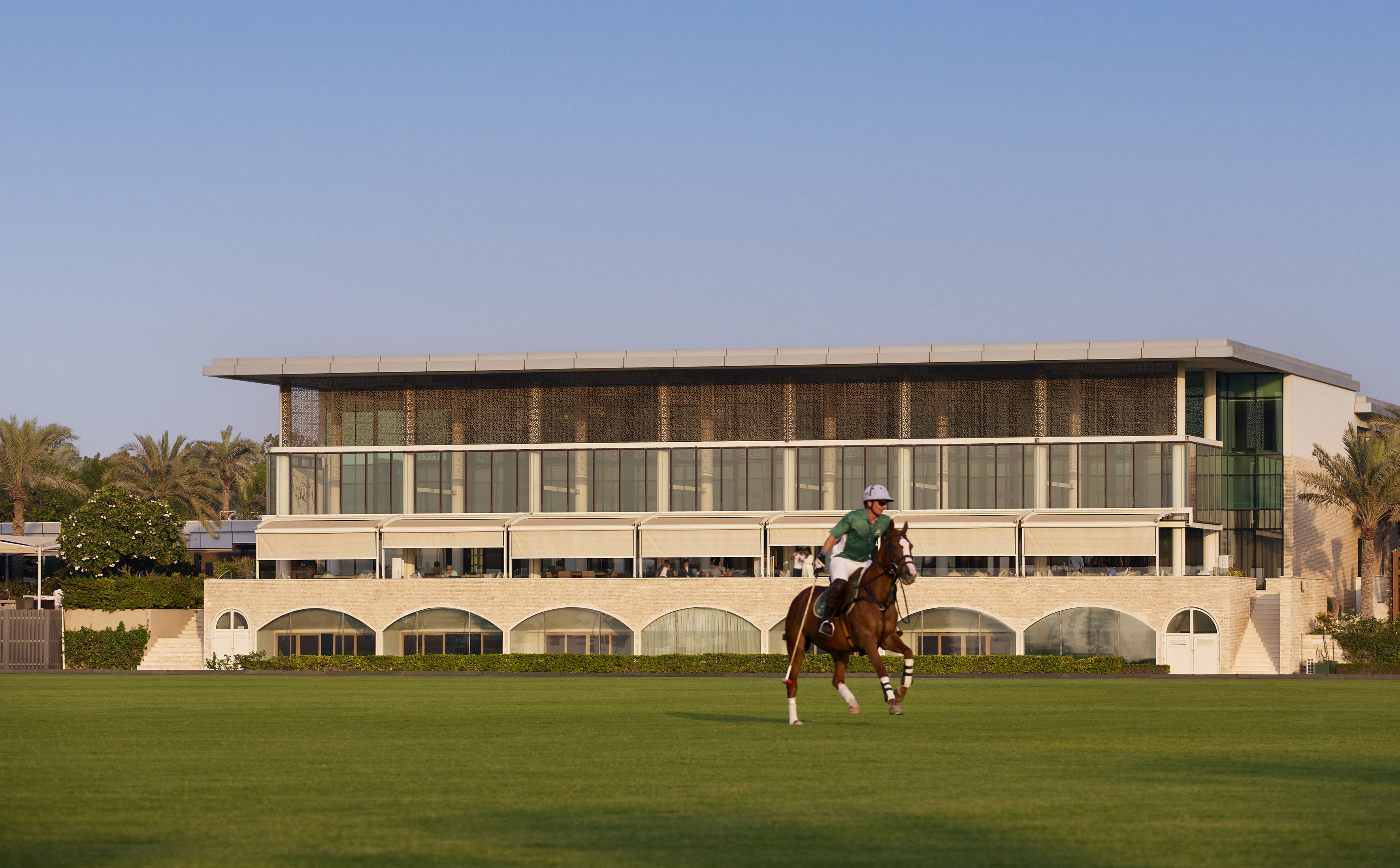 Polo player on horse, green field, modern luxury club building.