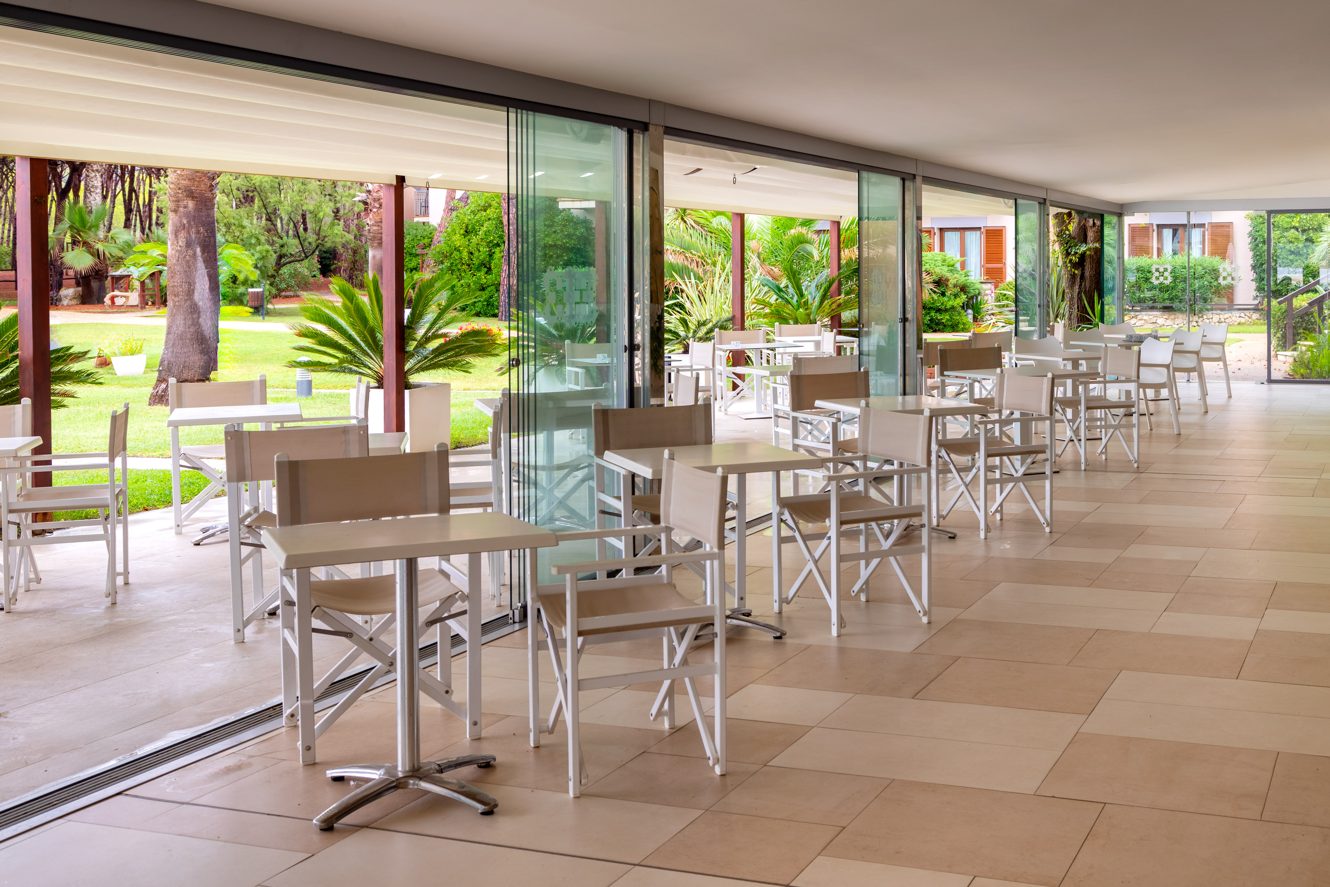 Resort patio dining area with white tables, chairs, and lush tropical garden view.