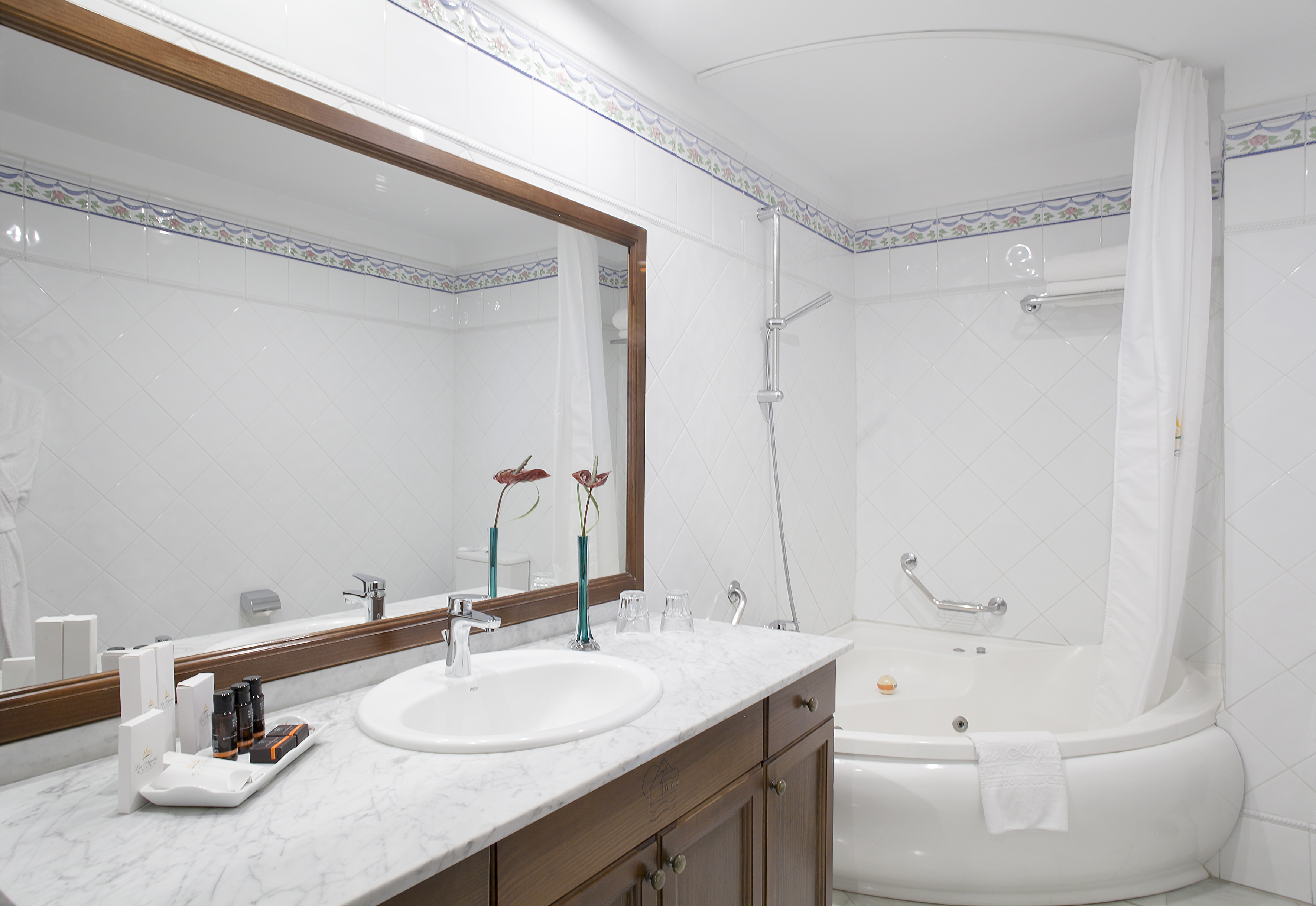 White tiled hotel bathroom with marble vanity, sink, mirror, and jacuzzi bathtub.