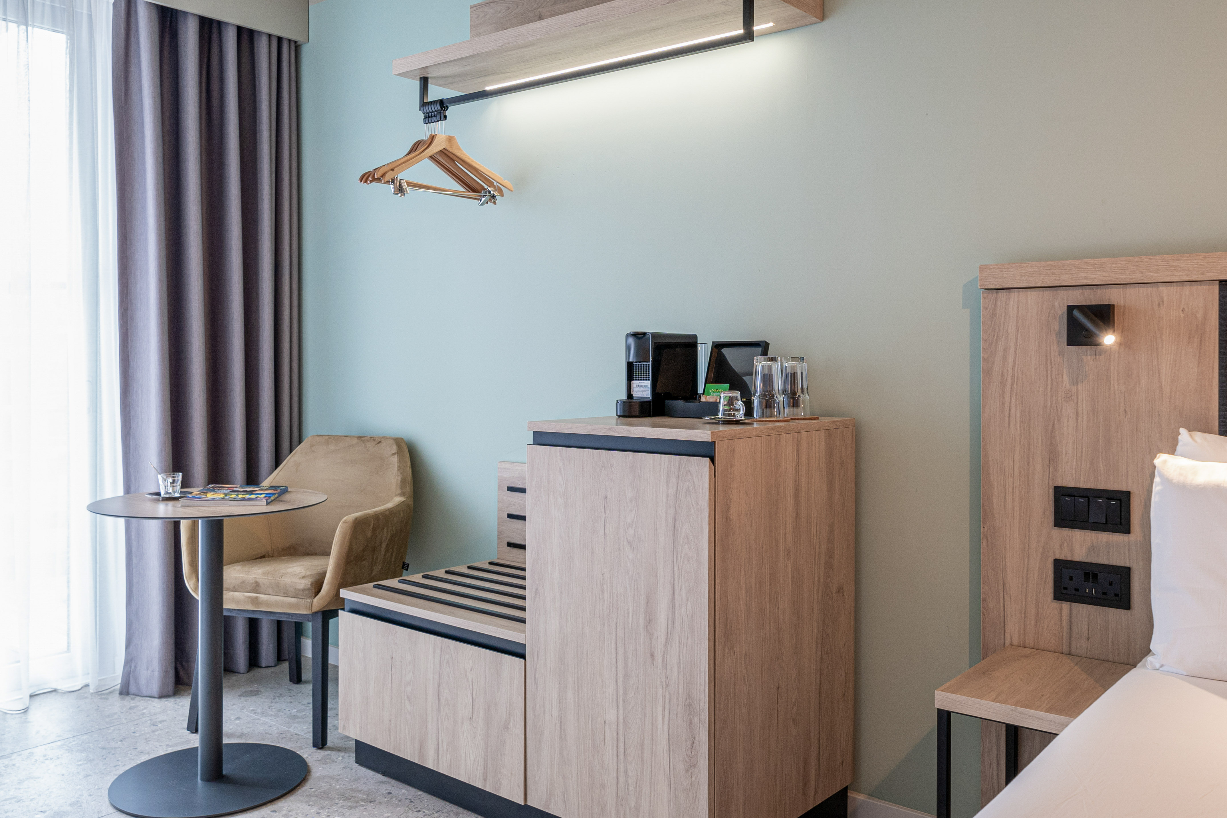 Modern hotel room featuring coffee maker, wooden storage, and compact seating.